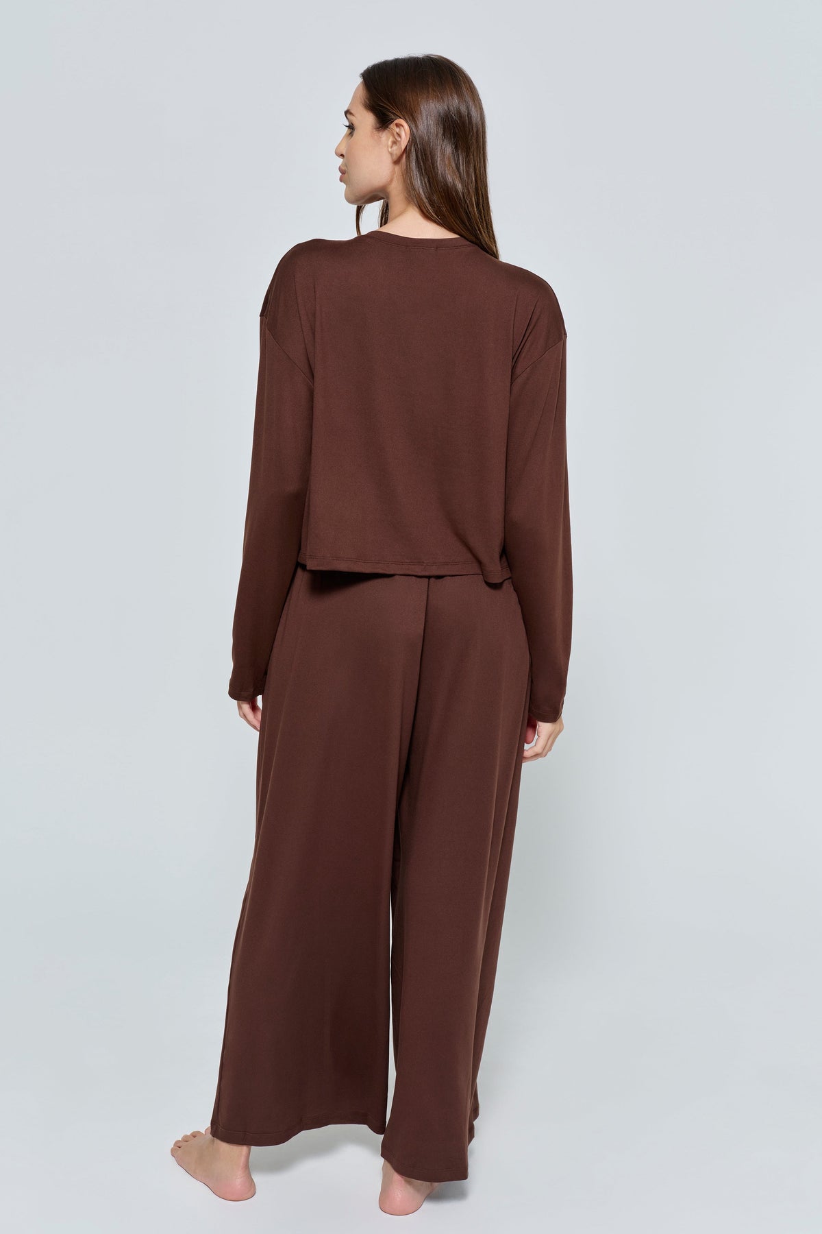 Back view of The Cloud Pant in chocolate showcasing its wide-leg floor-length fit on a model against a light gray background