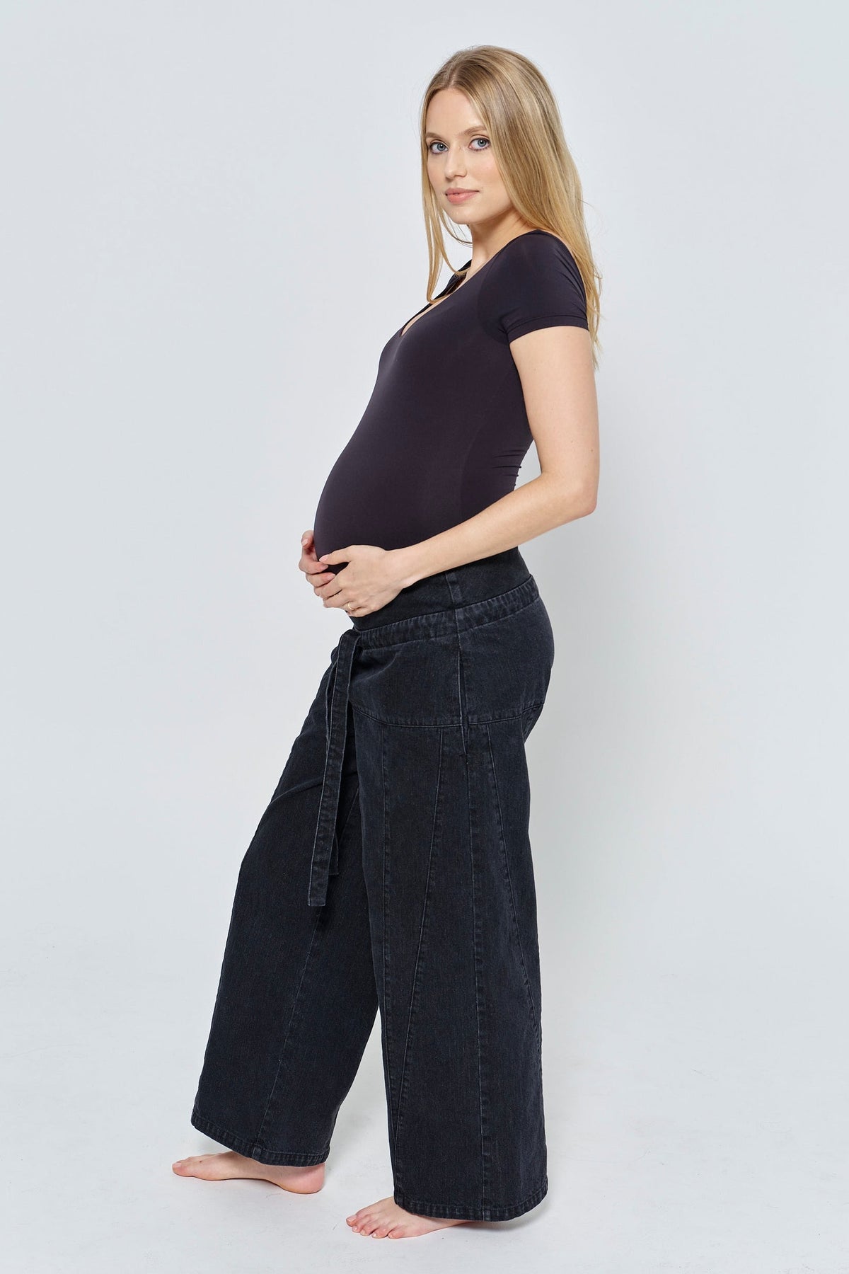 Side view of the relaxed denim jean in dark denim showcasing wide legs on a pregnant model with a light gray background