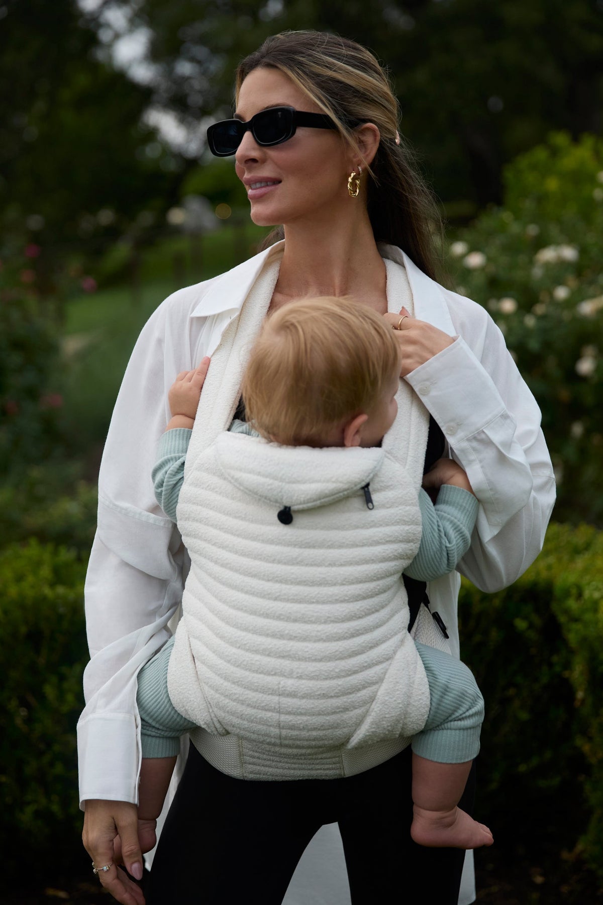 Woman wearing the Cloud Armadillo baby carrier with a child in a garden