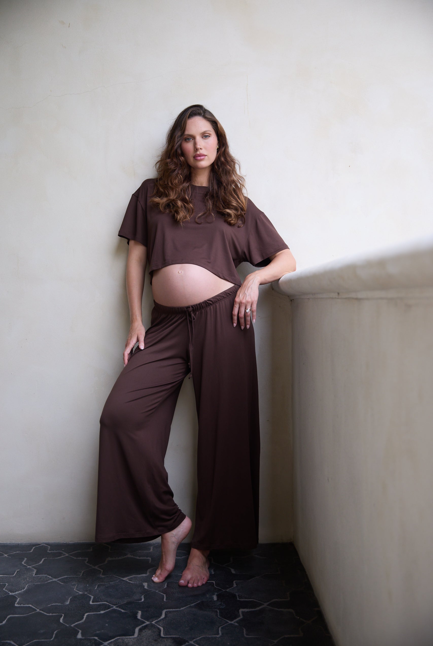 Woman in brown outfit standing against a plain wall.