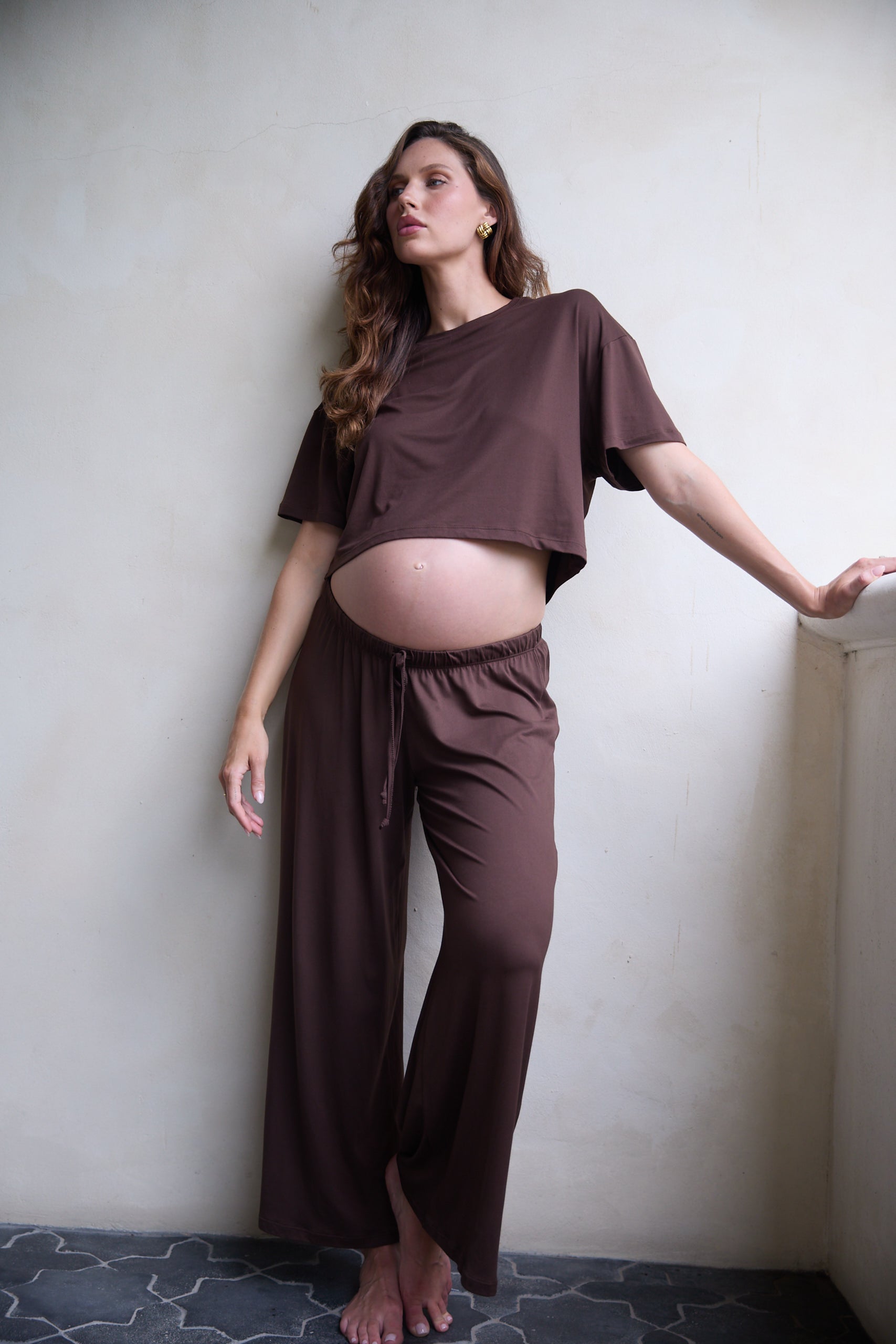 Pregnant woman wearing a brown outfit against a plain wall.