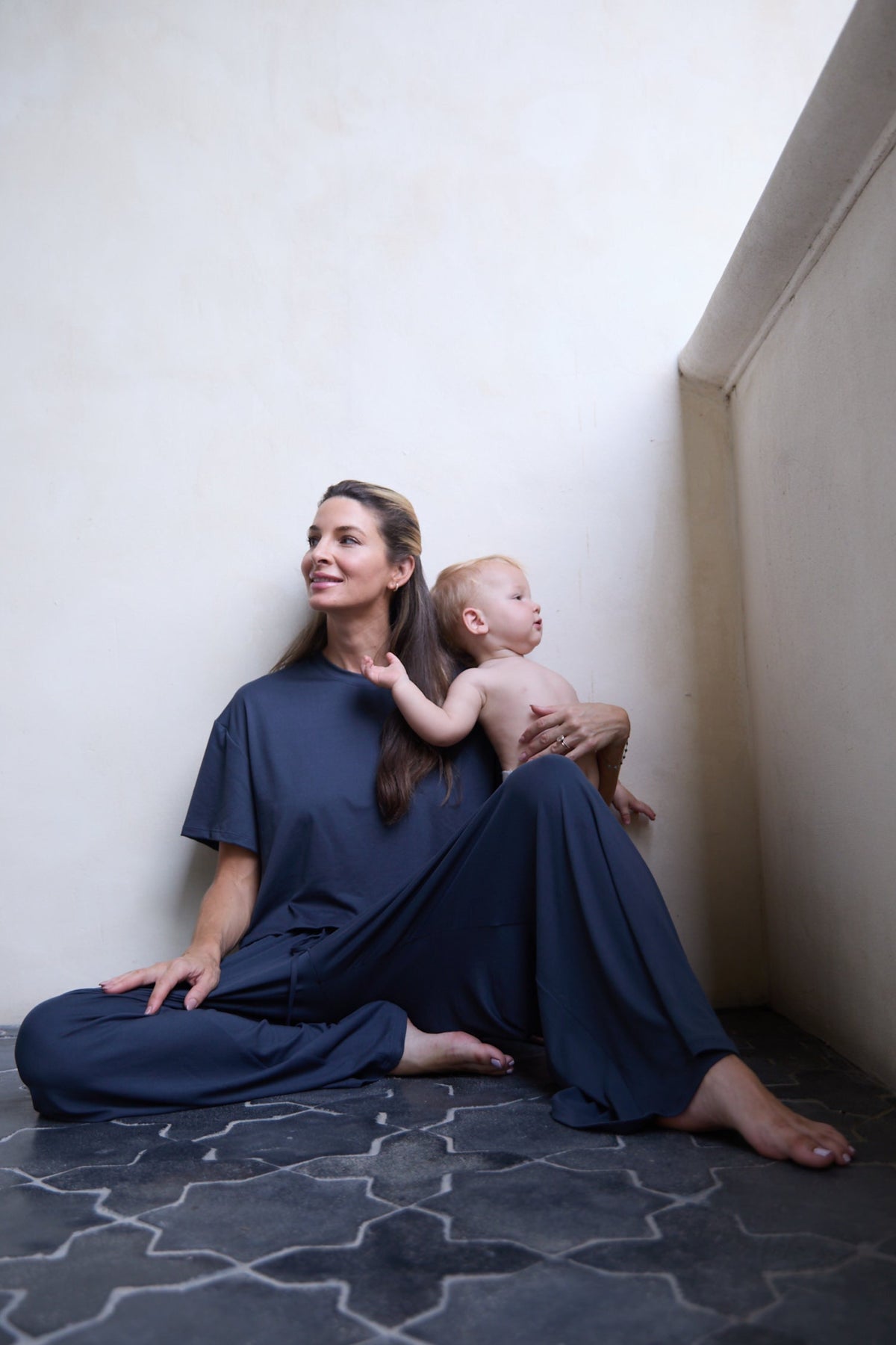 Woman holding a baby while wearing The Cloud Pant in a quiet home setting
