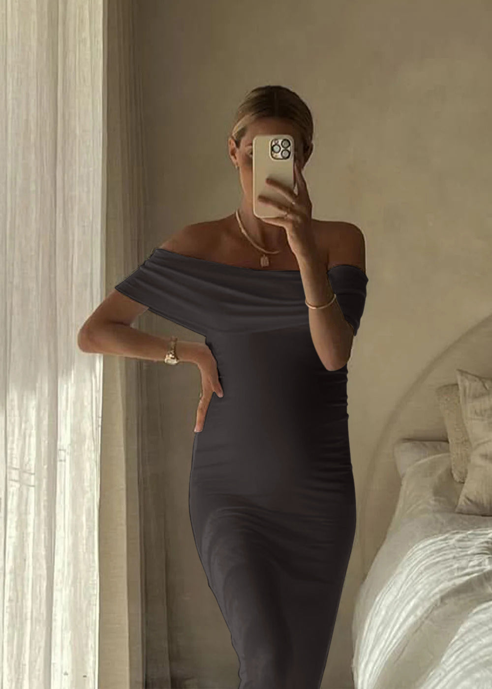 Pregnant woman taking a mirror selfie wearing an off-shoulder gray Bumpsuit dress in a bedroom.