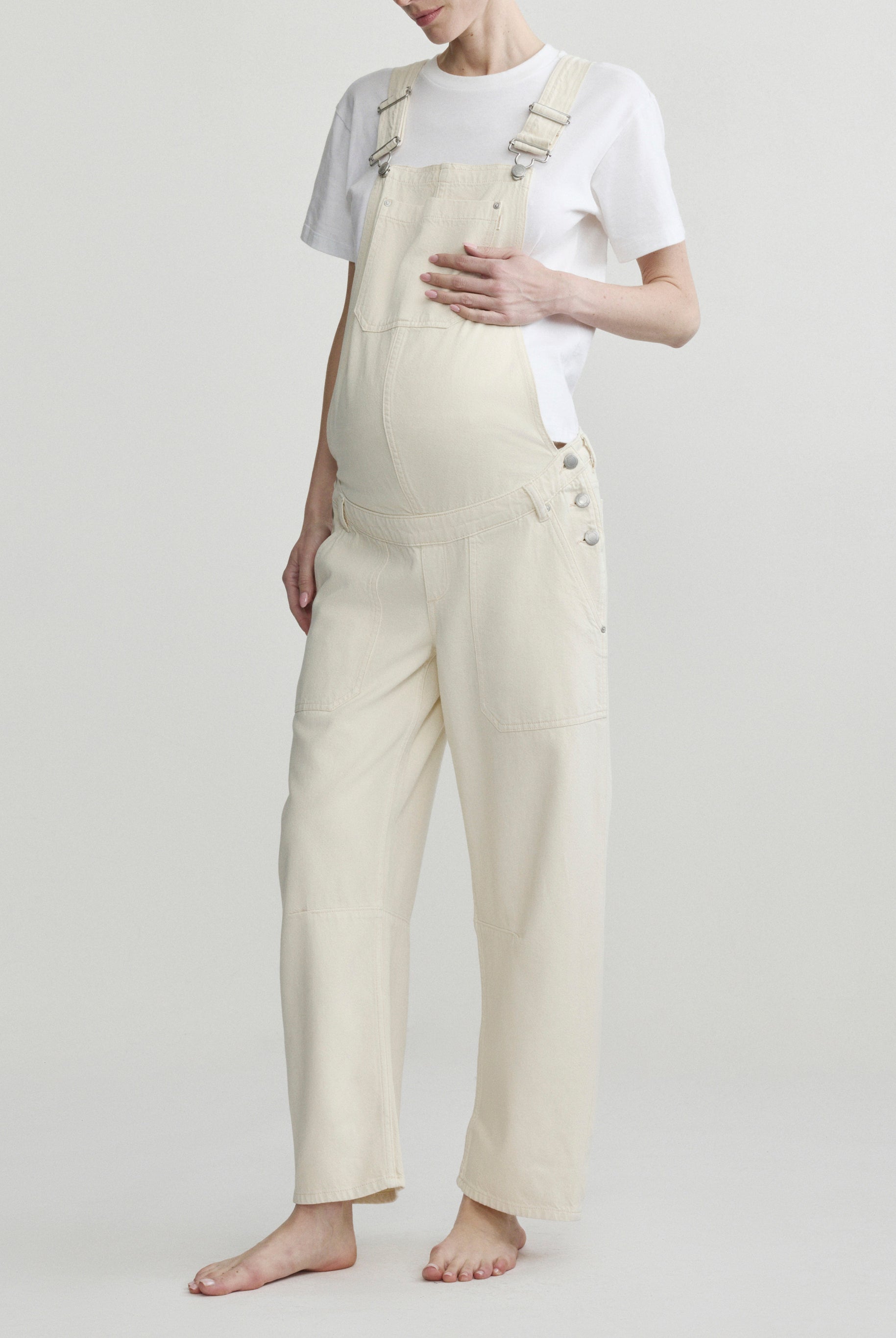 Pregnant woman wearing beige overalls on a plain background