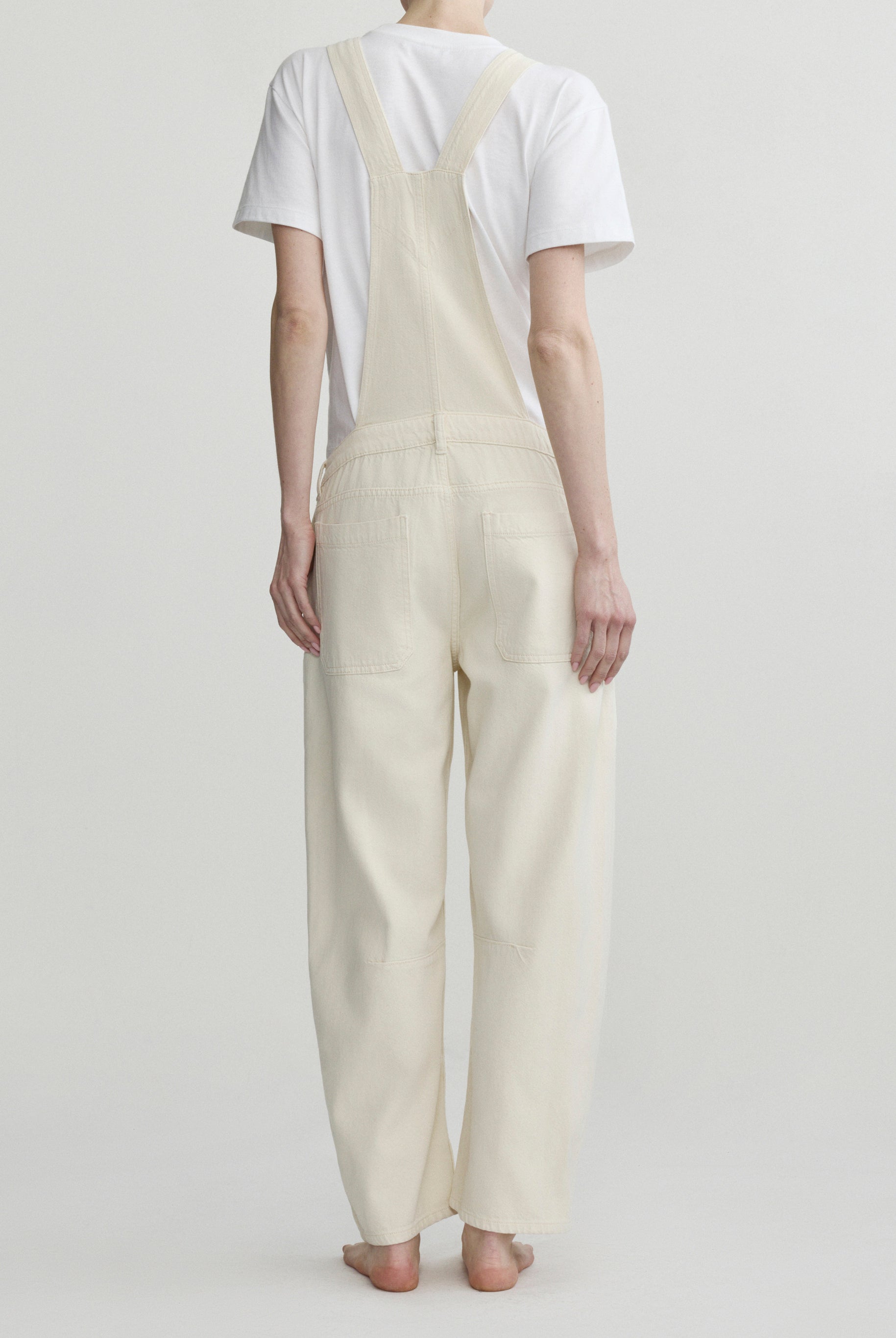 Person wearing cream-colored overalls and a white t-shirt on a plain background