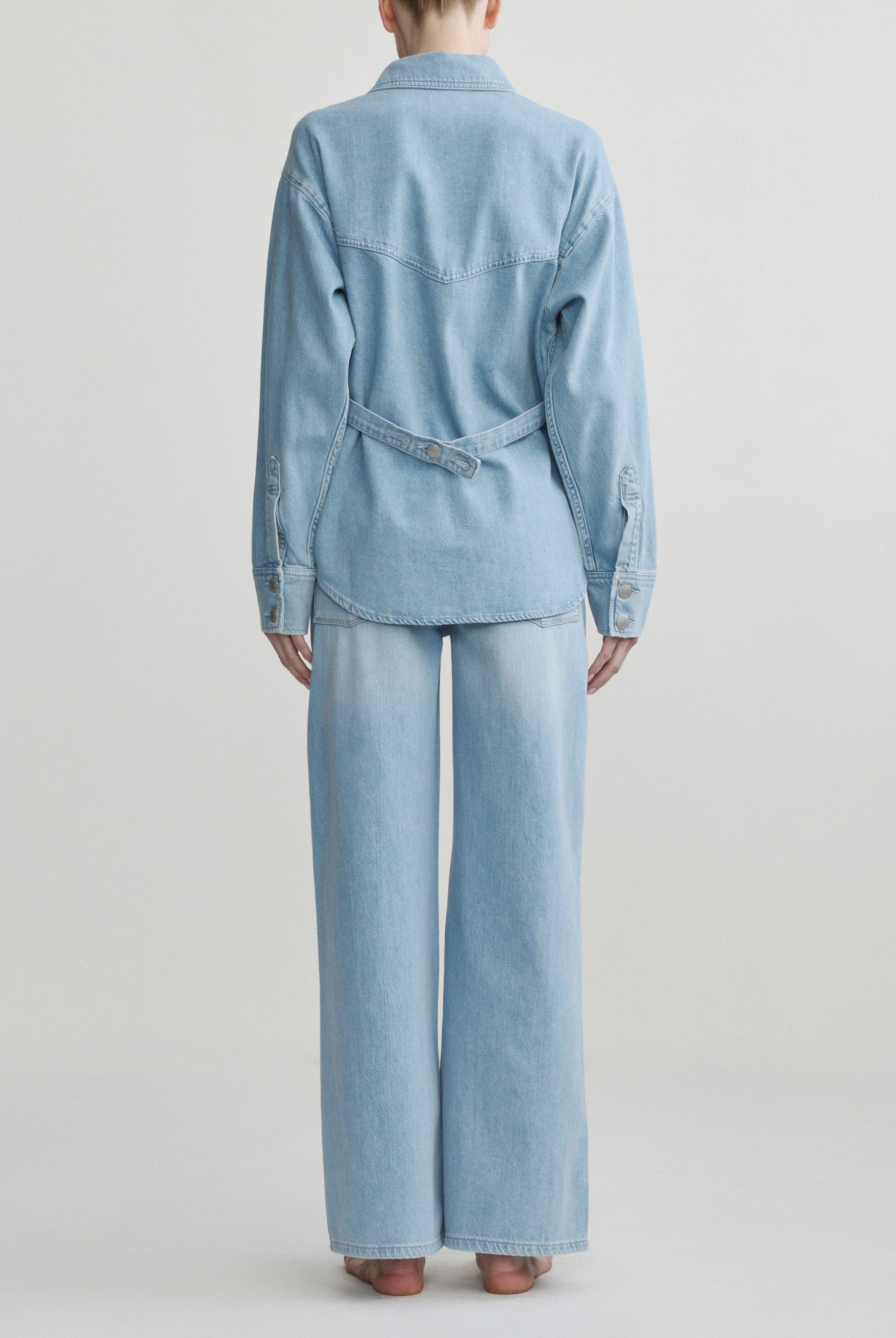 Person wearing a light blue denim outfit on a plain background