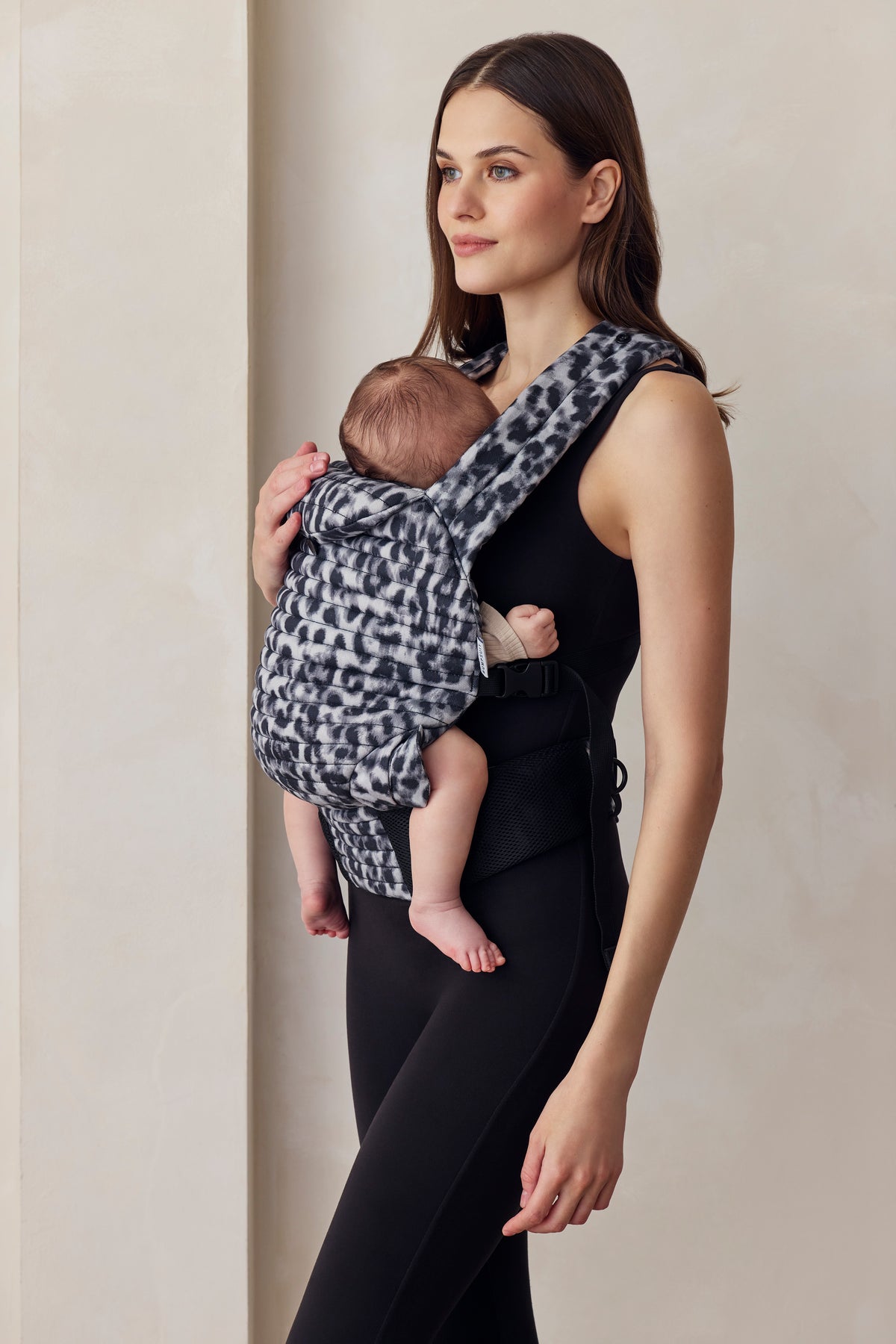 Woman holding a baby in a monochrome patterned carrier against a plain background