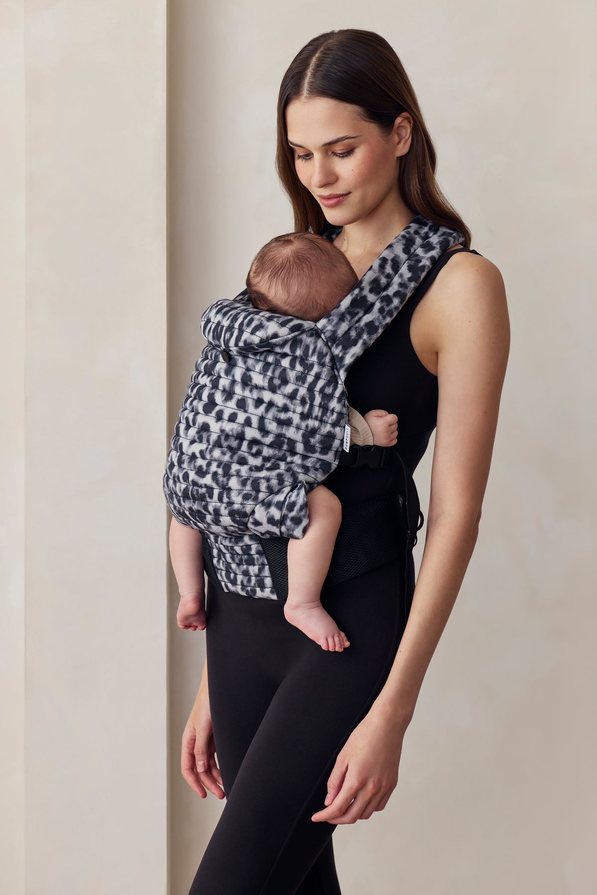 Woman holding a baby in a monochrome baby carrier against a plain background