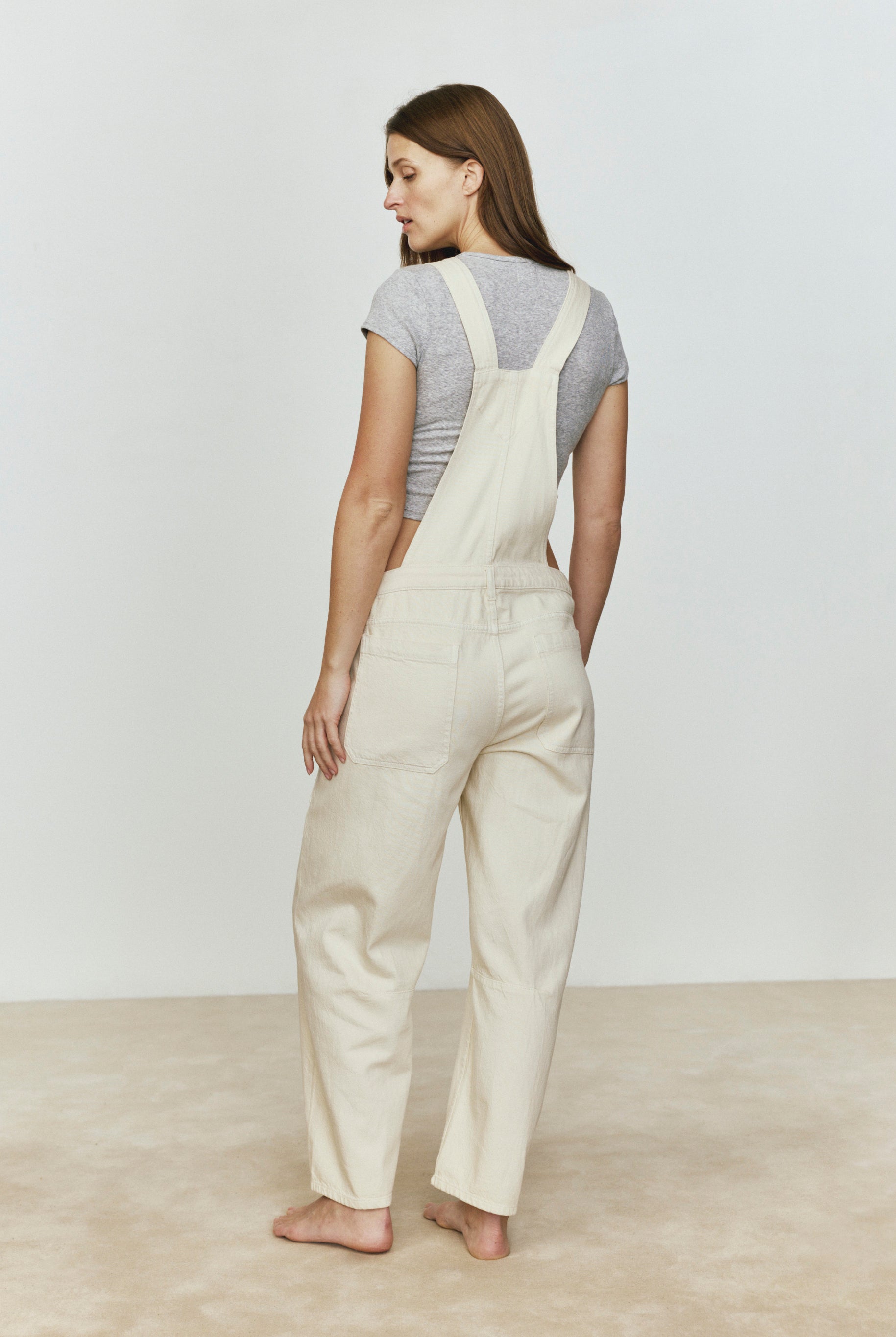 Woman wearing beige overalls against a plain background