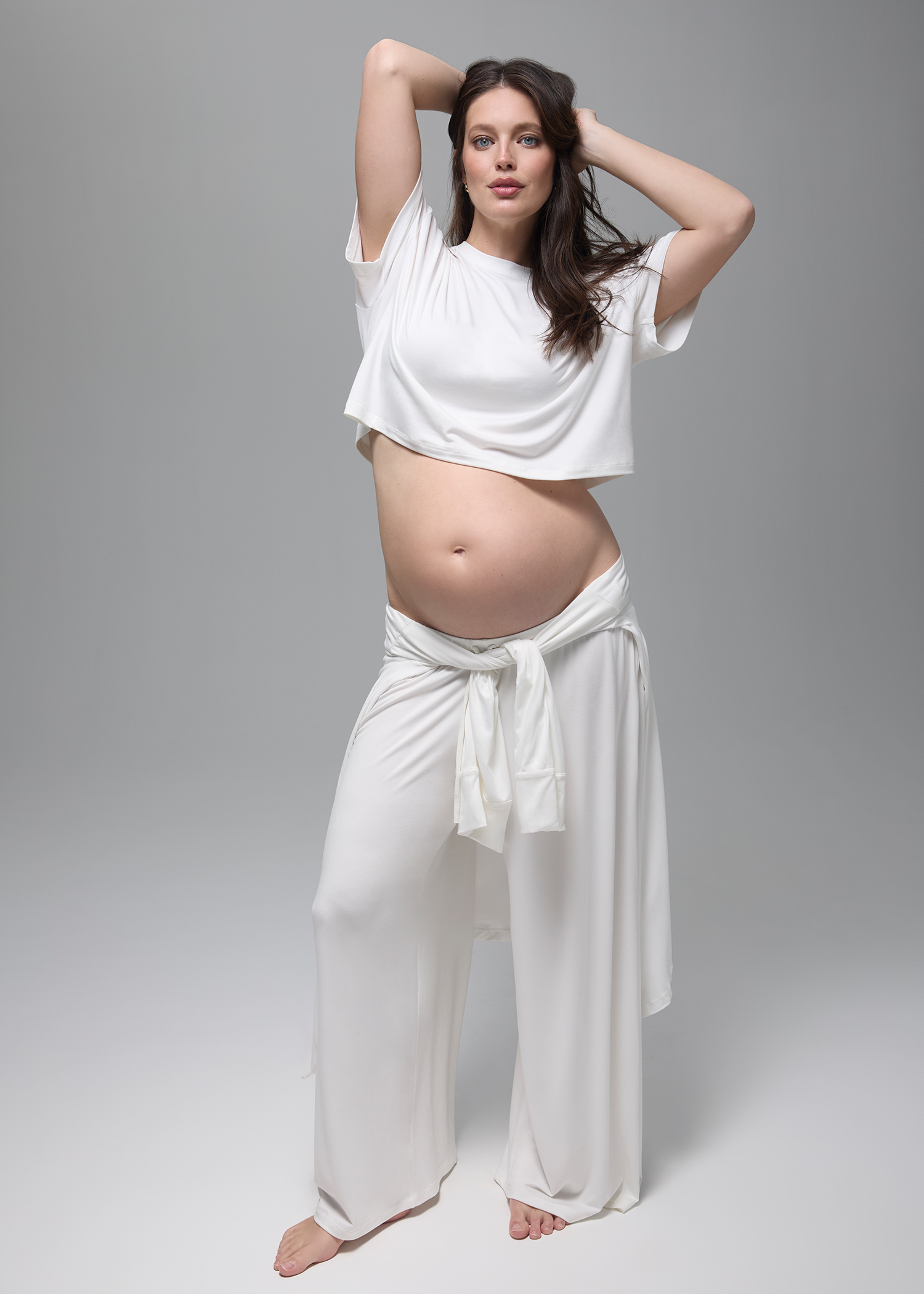 Pregnant woman wearing a white bumpsuit outfit on a gray background