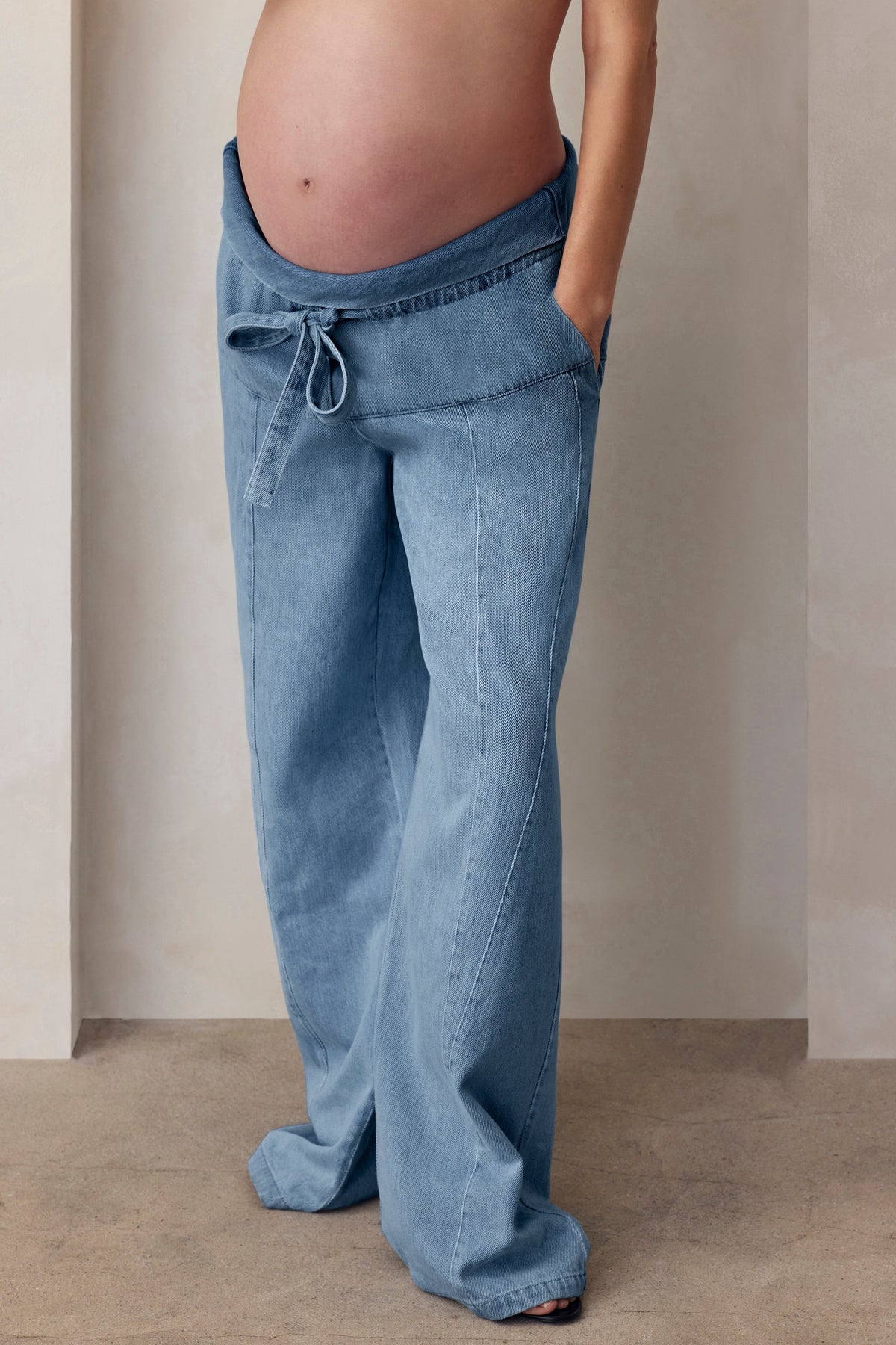 Side view of relaxed maternity painter jeans in light blue denim showcasing a drawstring waist and wide legs against a neutral background