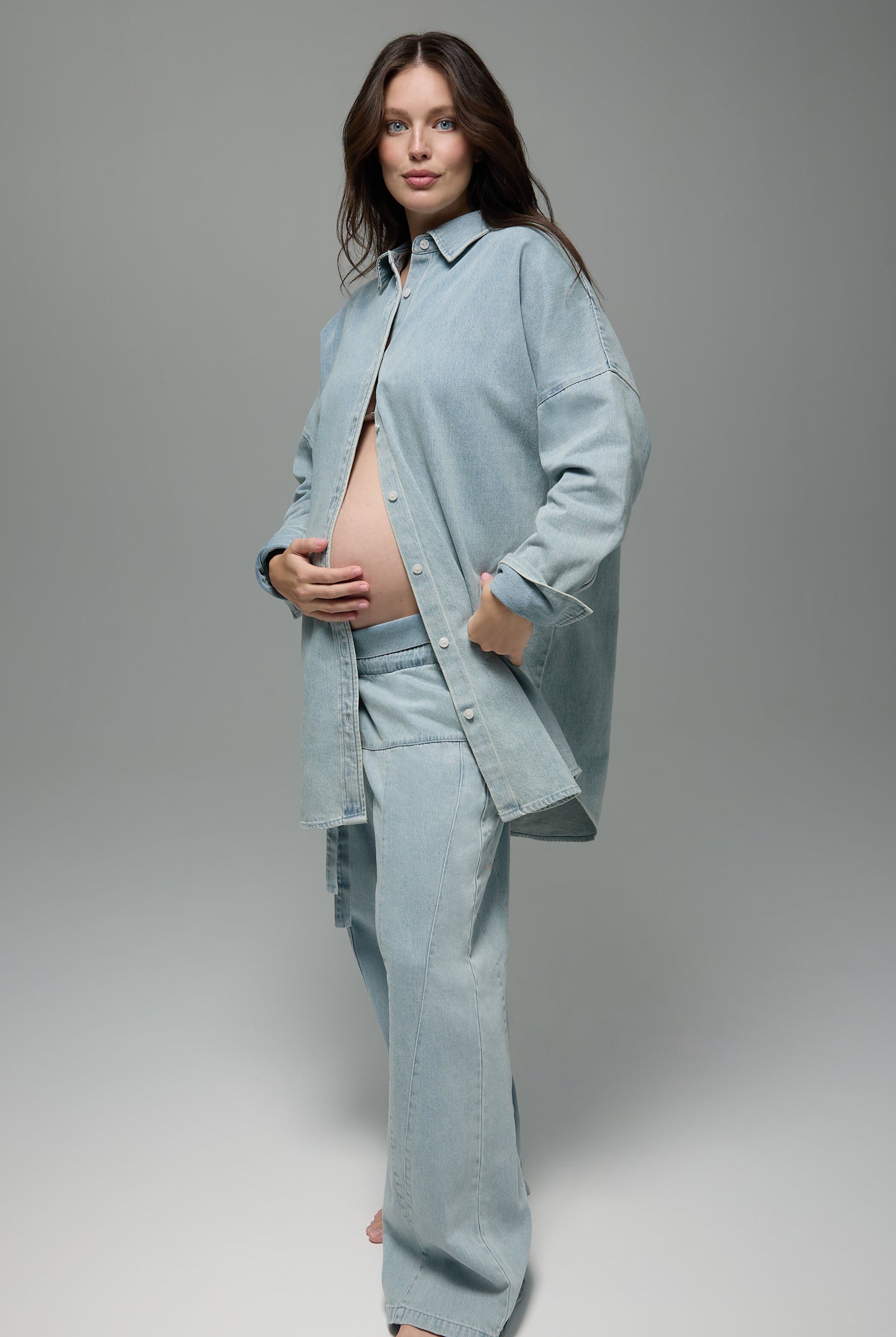 Pregnant women wearing a Bumpsuit denim jeans and denim shirt against a grey background