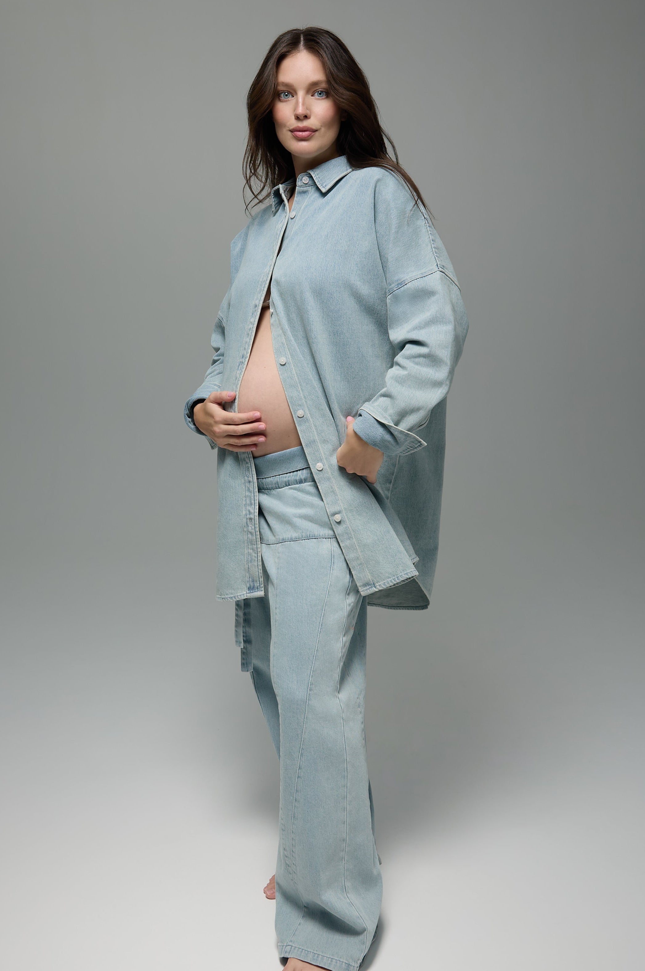 Pregnant women wearing a Bumpsuit denim jeans and denim shirt against a grey background