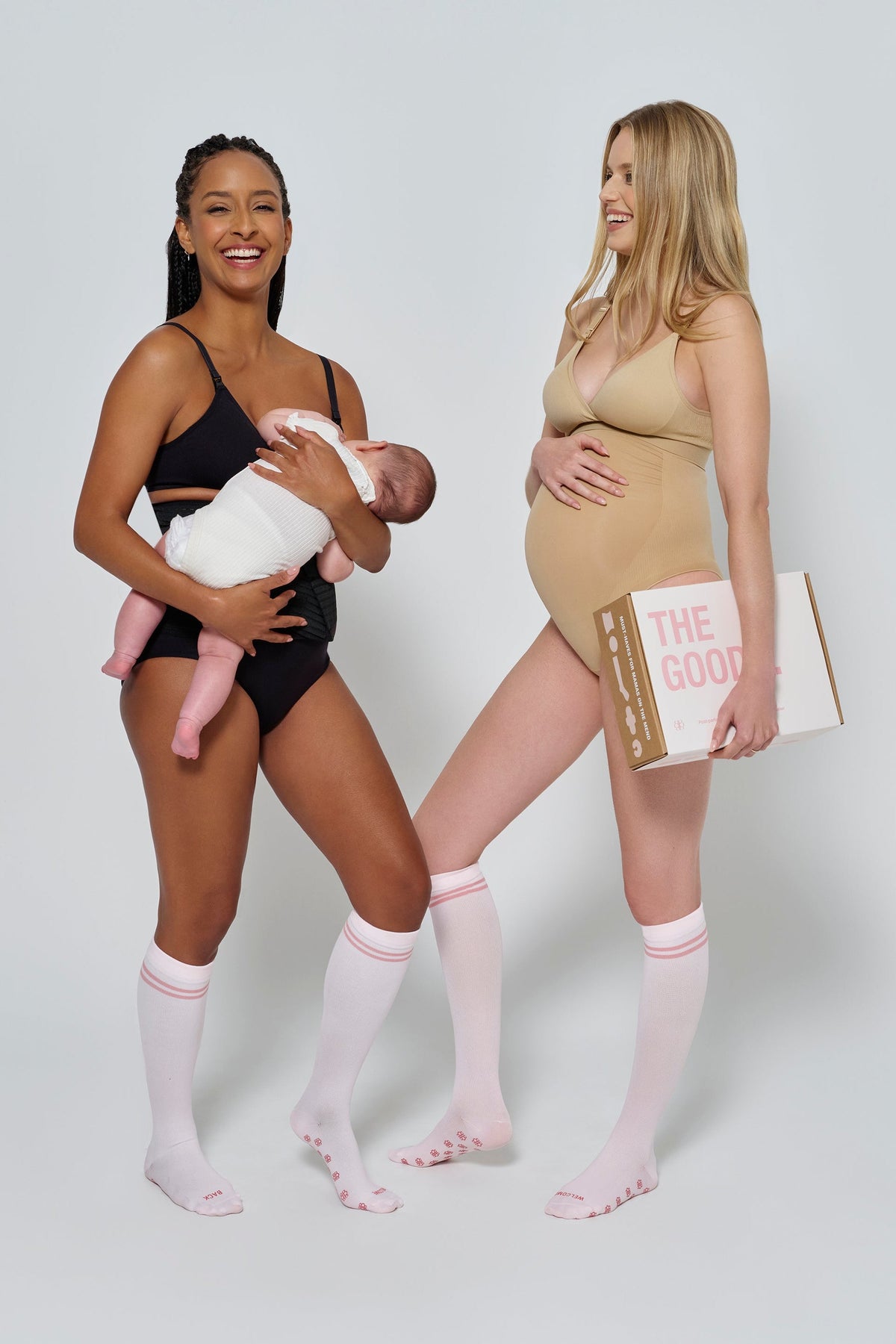 A woman holds a baby while a pregnant woman holds a postpartum care book in a studio
