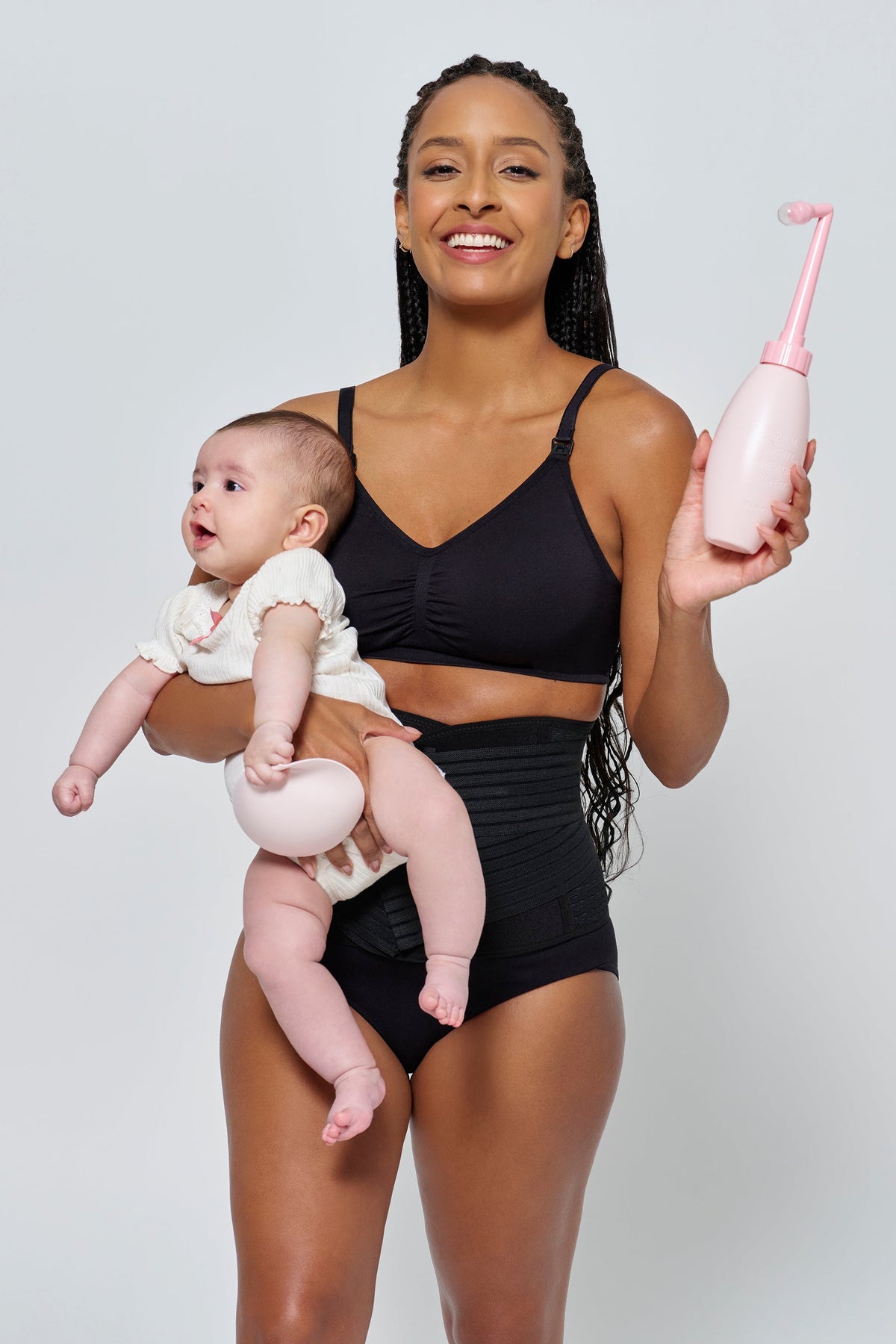Front view of Ice Pink NO-STING SPRITZ peri bottle with angled spray spout, held by a woman carrying a baby on a gray background