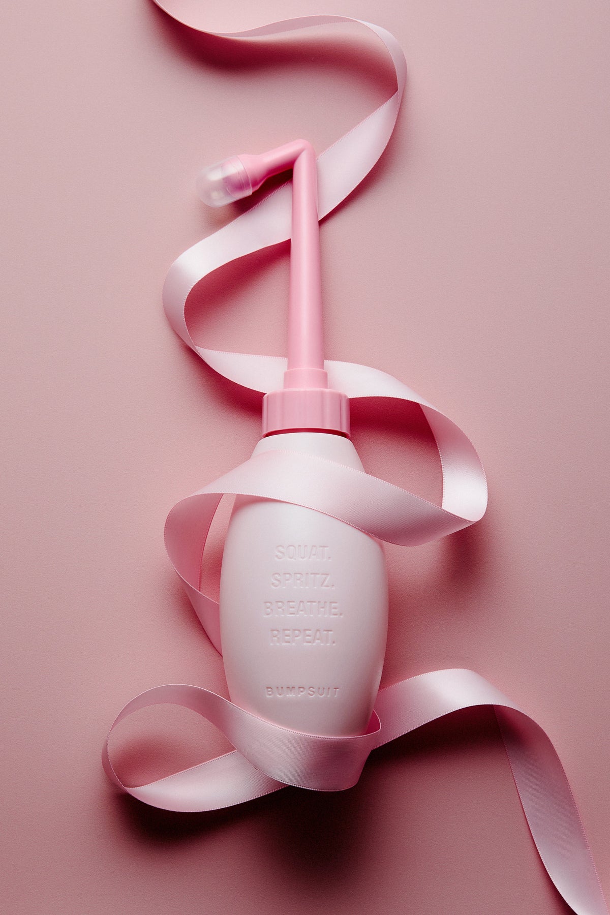 Close-up of the Ice Pink NO STING SPRITZ peri bottle showcasing its angled spray nozzle with a pink ribbon background