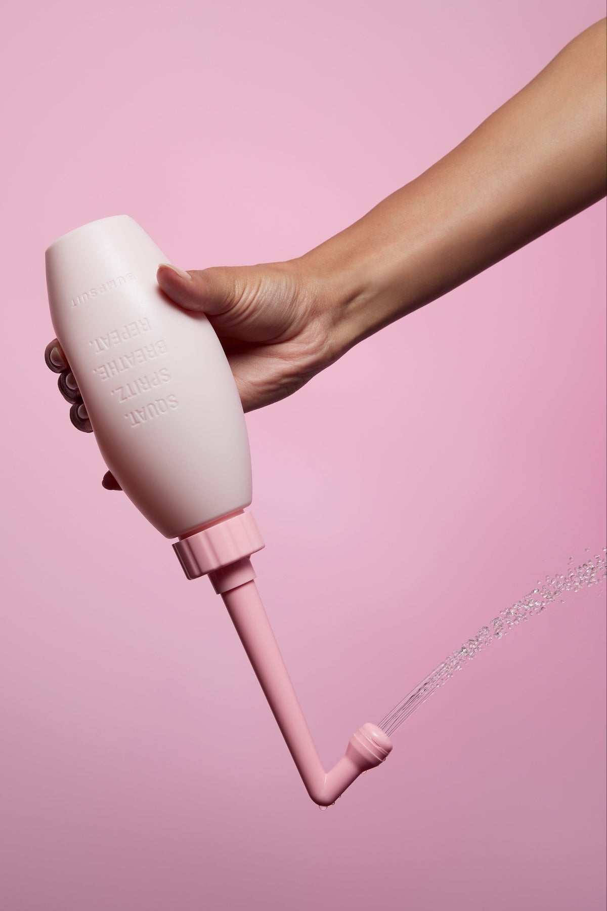 Close-up of NO-STING SPRITZ peri bottle showcasing its angled spray in use against a pink background