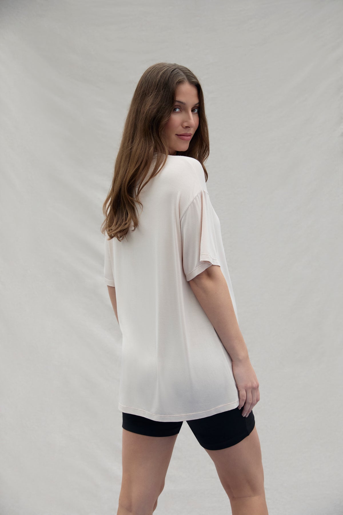 Woman wearing a oat oversized shirt and black shorts on a plain background