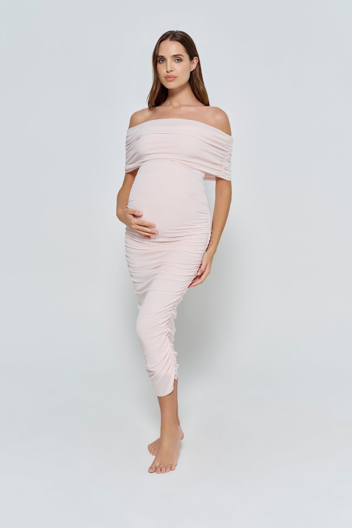 Woman wearing a light pink mesh off-shoulder dress against a white background