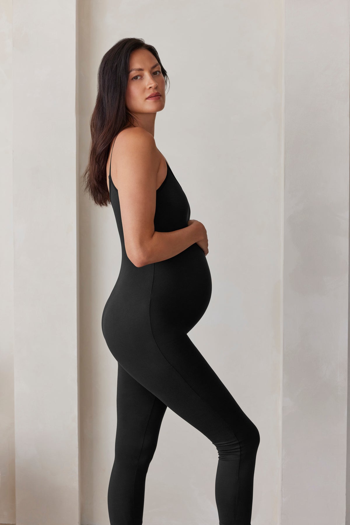 Woman wearing a black sleeveless jumpsuit The Kate standing against a plain background