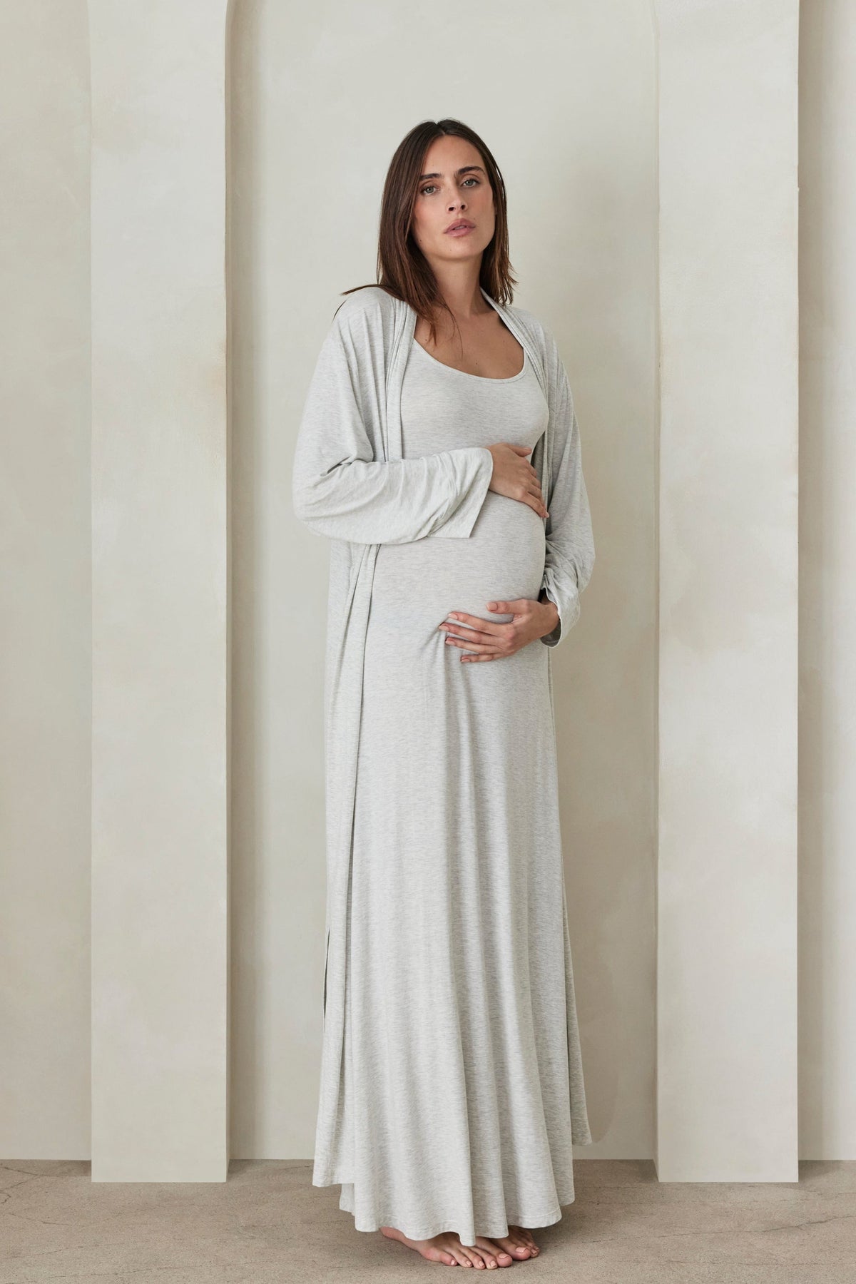 Full view of The Cloud Dress in Heather Grey showcasing its floor-length fit on a pregnant model in a neutral room