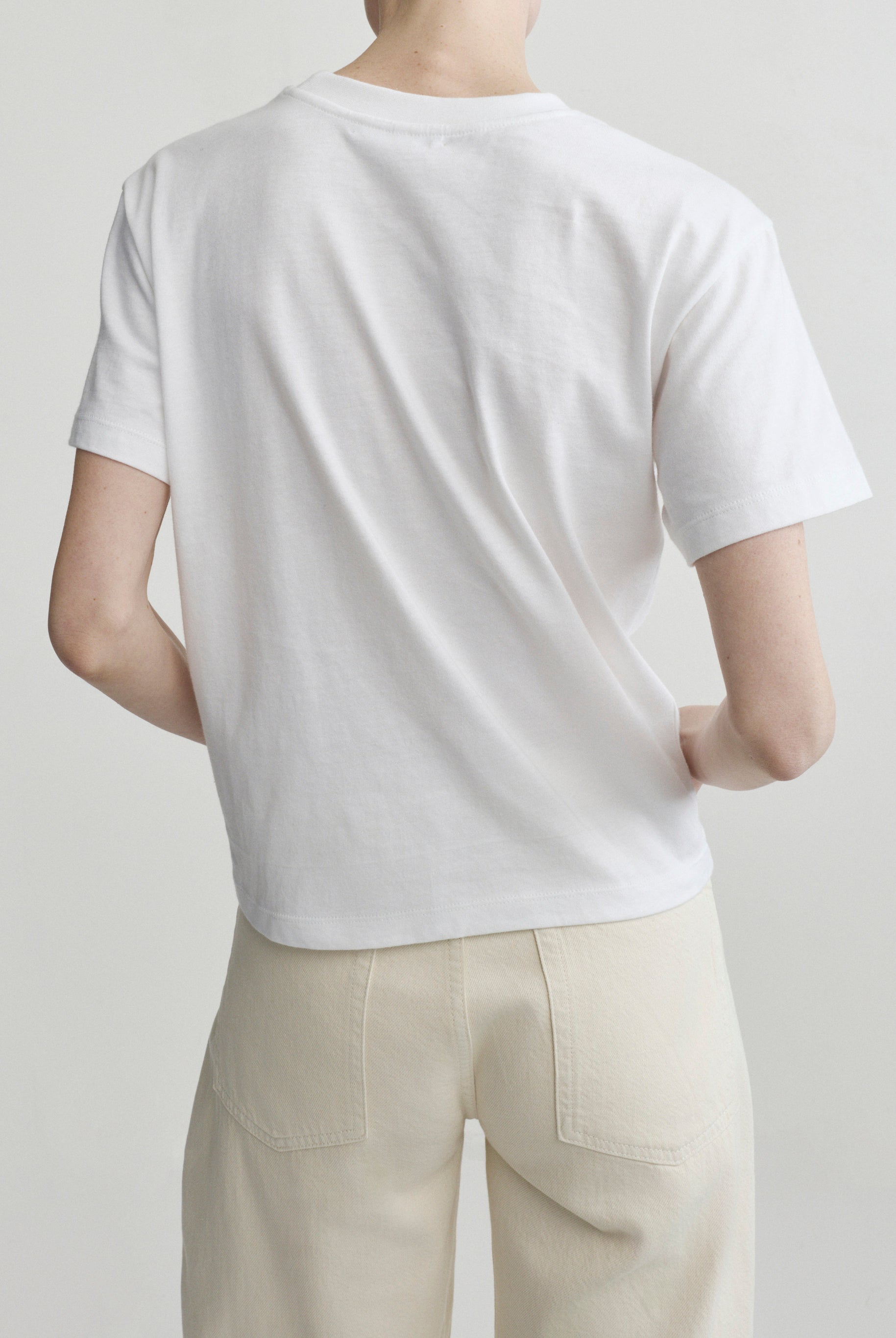 Person wearing a plain white t-shirt and beige pants on a light gray background