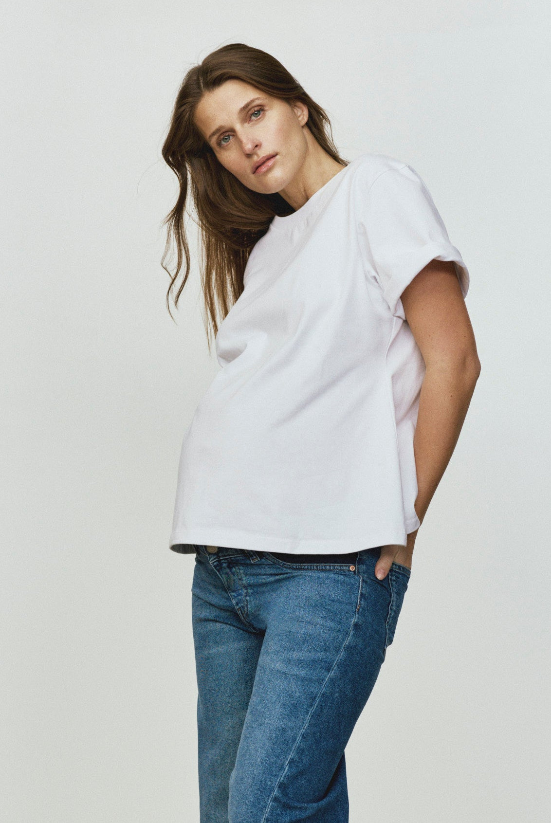 Woman wearing a white top and blue jeans standing against a plain background