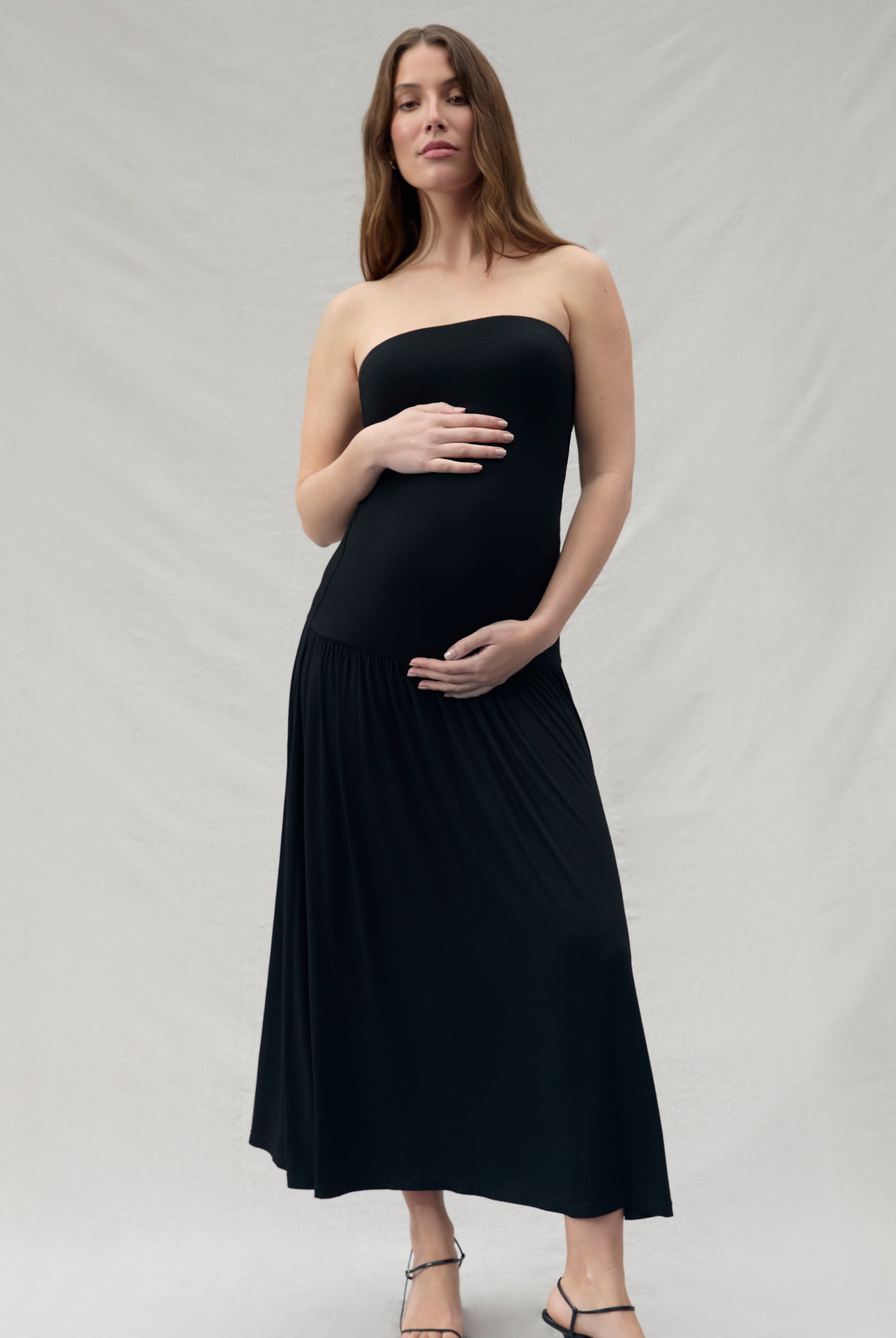 Pregnant woman wearing a black strapless dress on a plain background