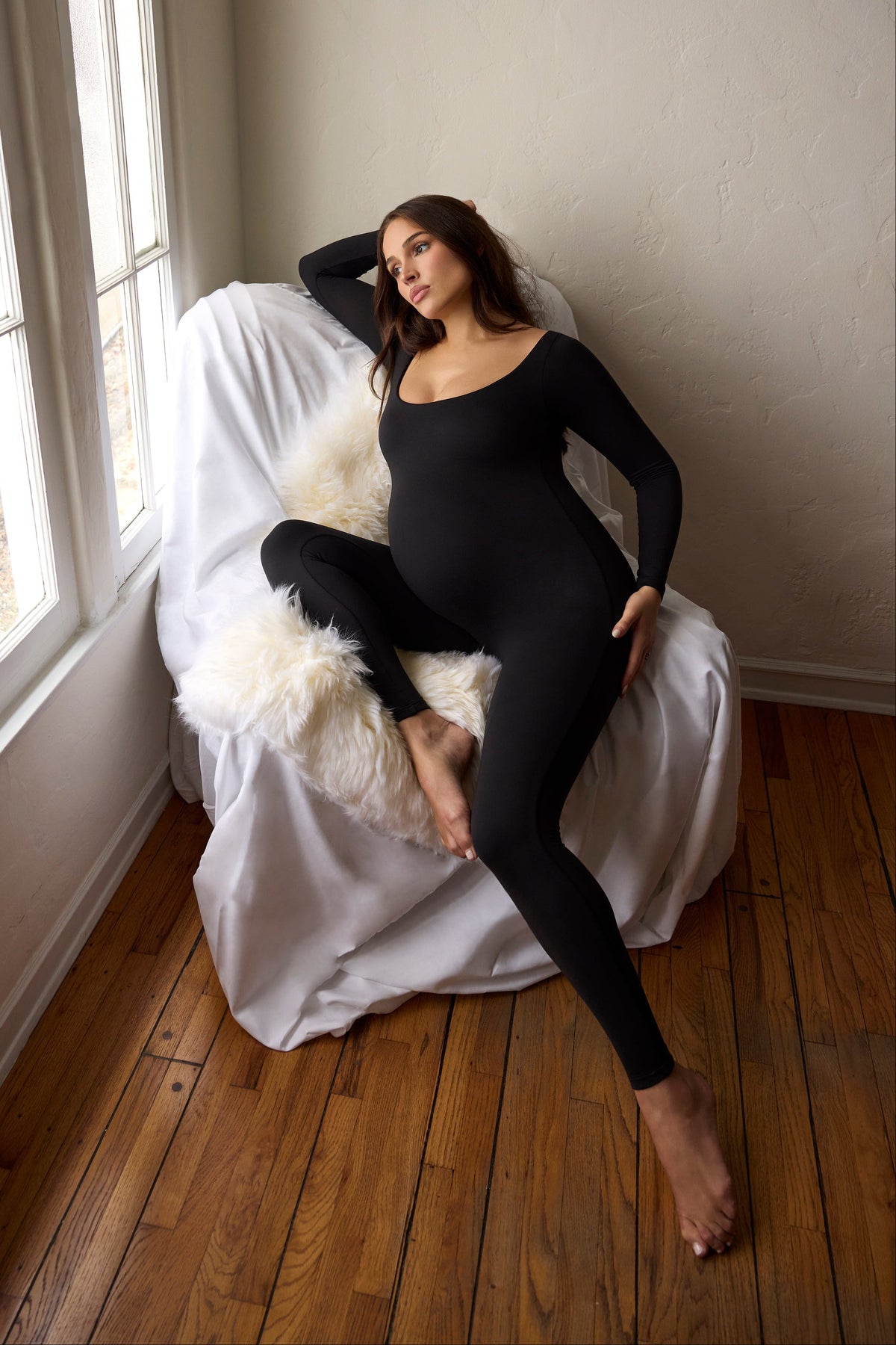 Front view of the Celine Scoop Neck Unitard showcasing its black color and close fit on a seated pregnant model