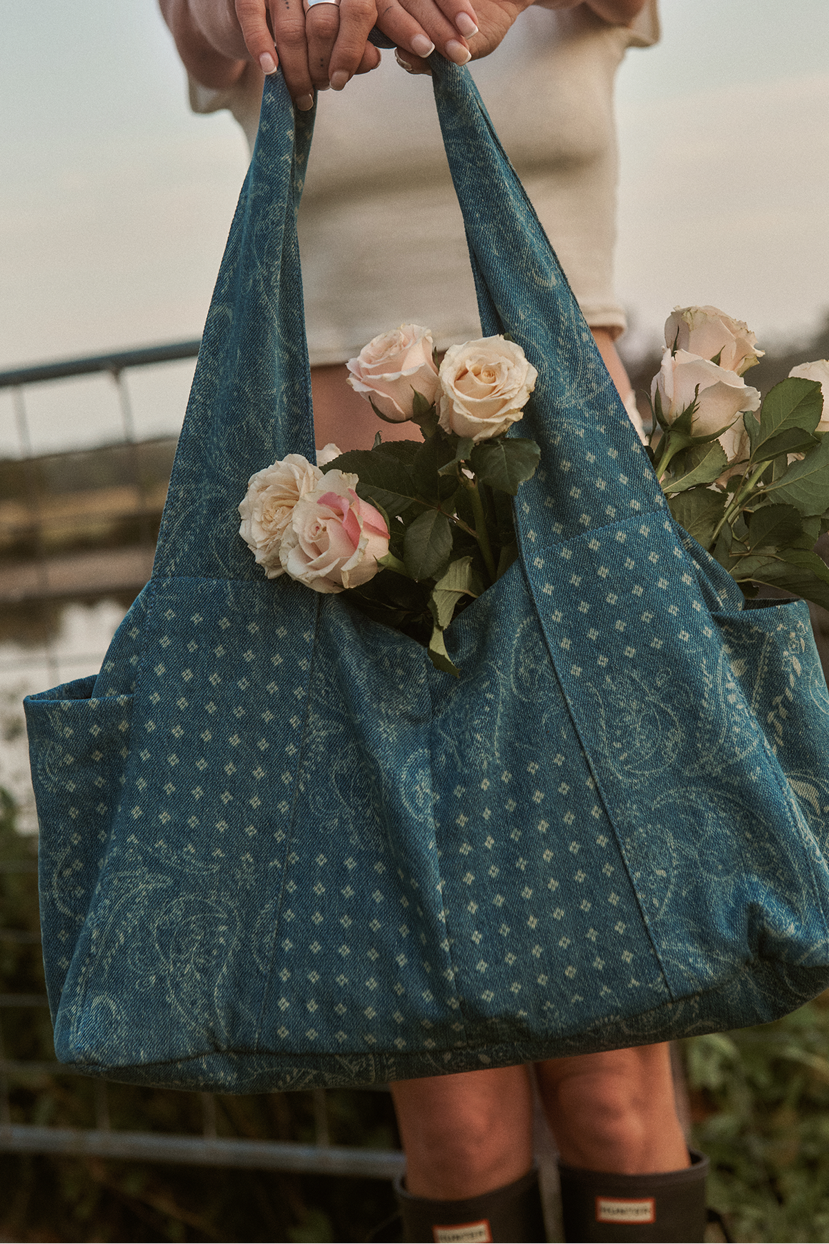 Front view of The Diaper Bag showcasing the Roadtrip Denim print with roses inside and an outdoor waterside background