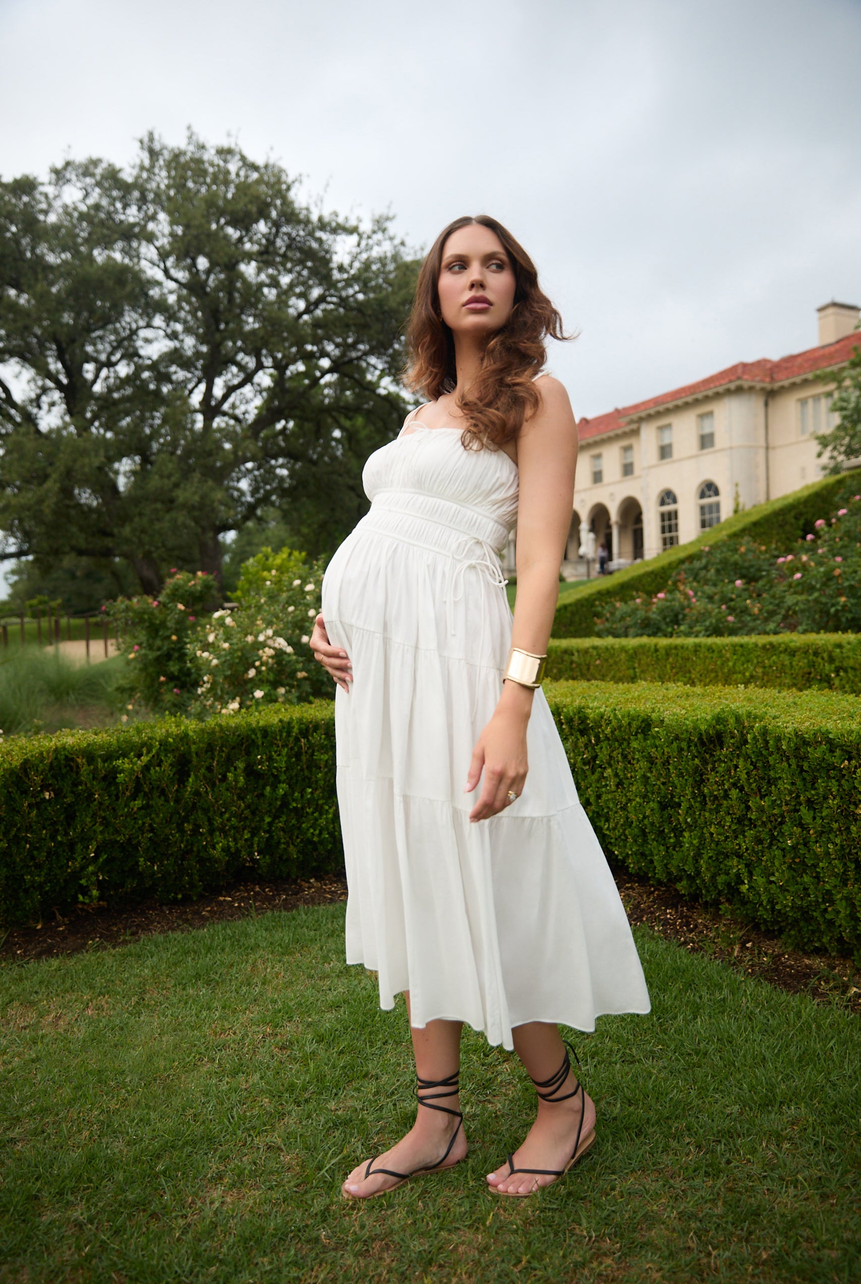 Pregnant woman in a white dress standing in a garden.