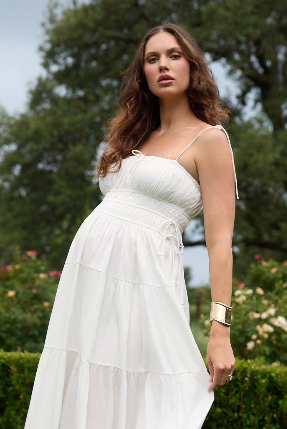 Woman in a white dress standing outdoors with greenery in the background