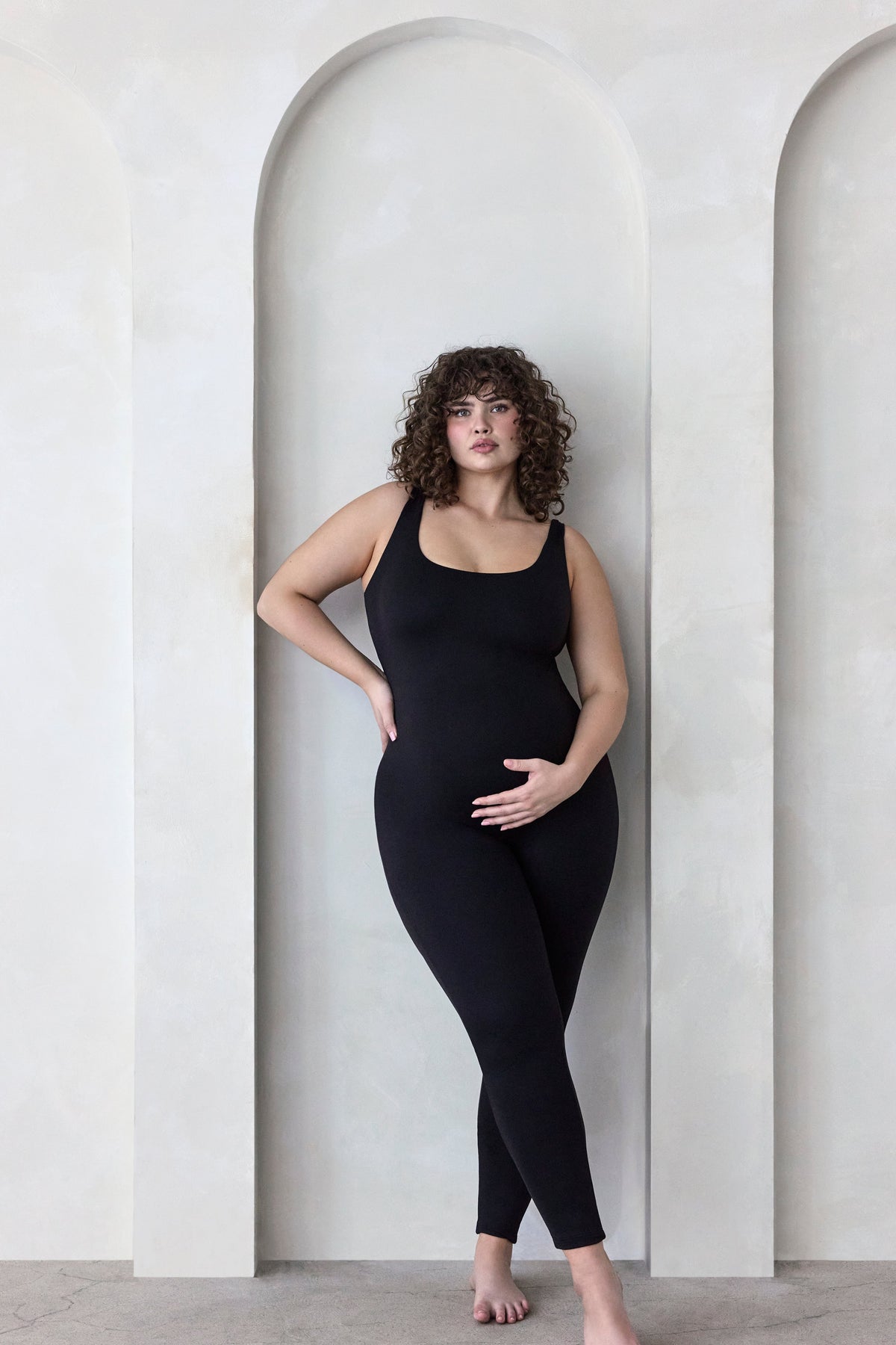Front view of The Cotton Lucy maternity unitard in black with scoop neckline and wide straps on a model