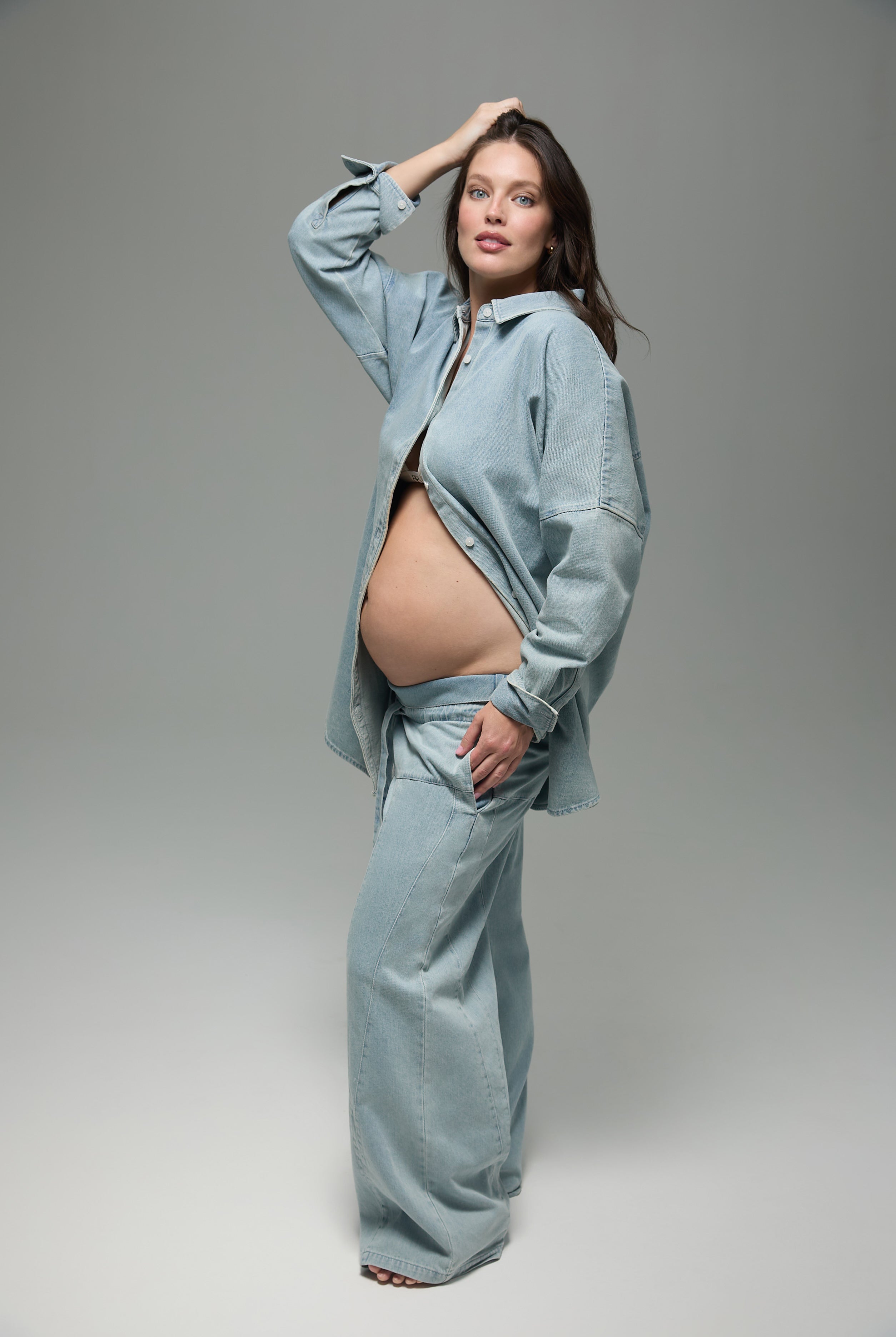 Pregnant woman wearing a matching denim outfit on a gray background