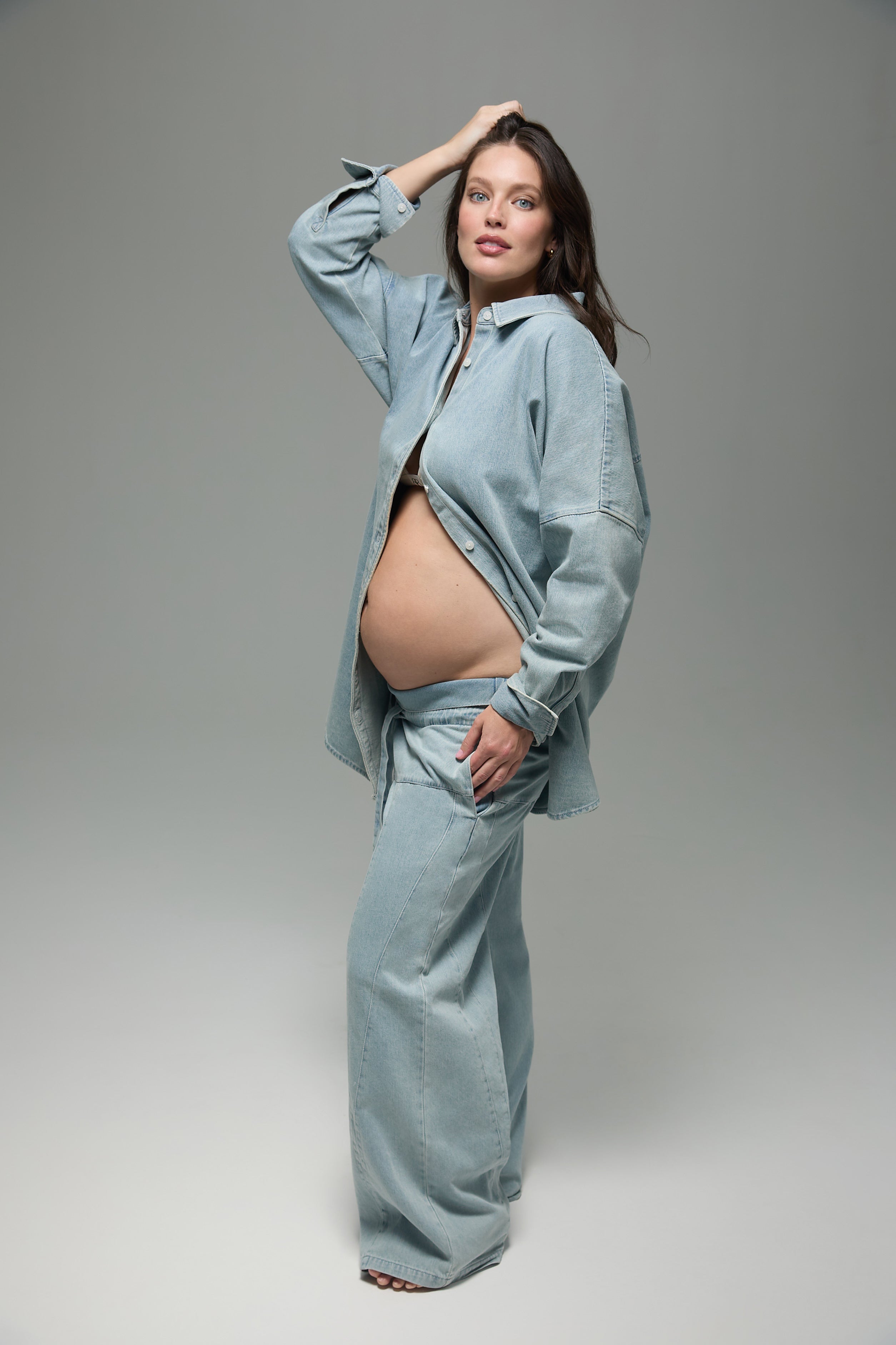 Pregnant woman wearing a matching denim outfit on a gray background