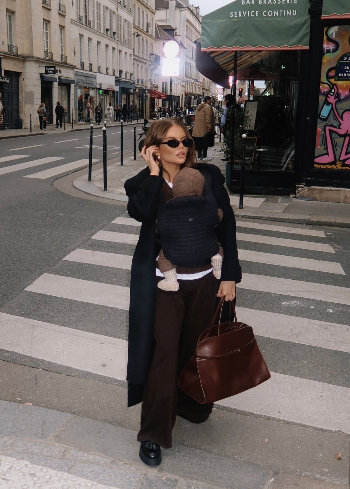 model walking in the streets wearing the armadillo baby carrier in black