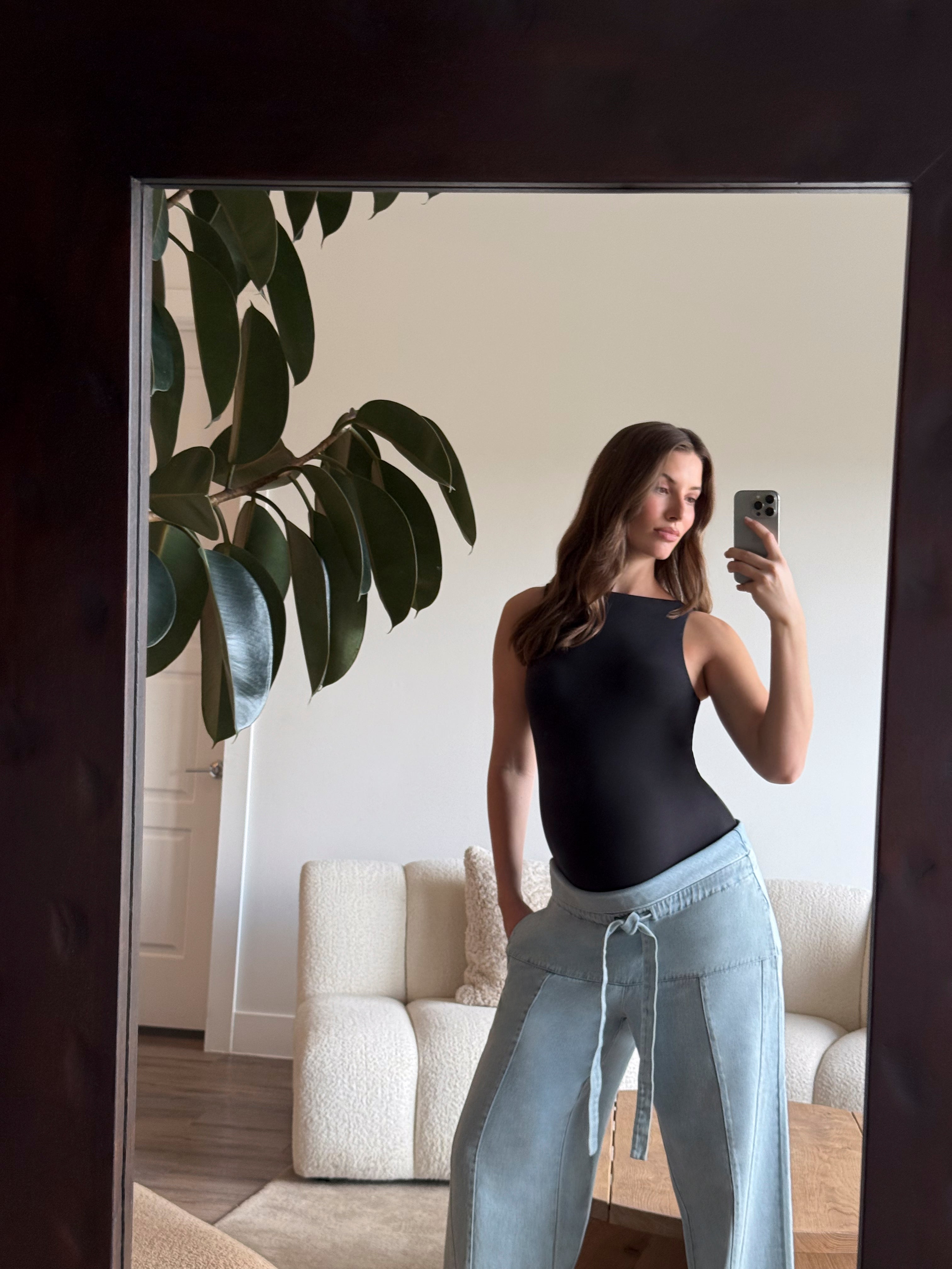 pregnant person taking a mirror selfie wearing Bumpsuitsblack boatneck bodysuit and jeans