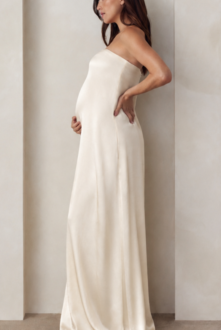 Side view of a pregnant woman wearing a Bumpsuit brushed satin gown in champagne color