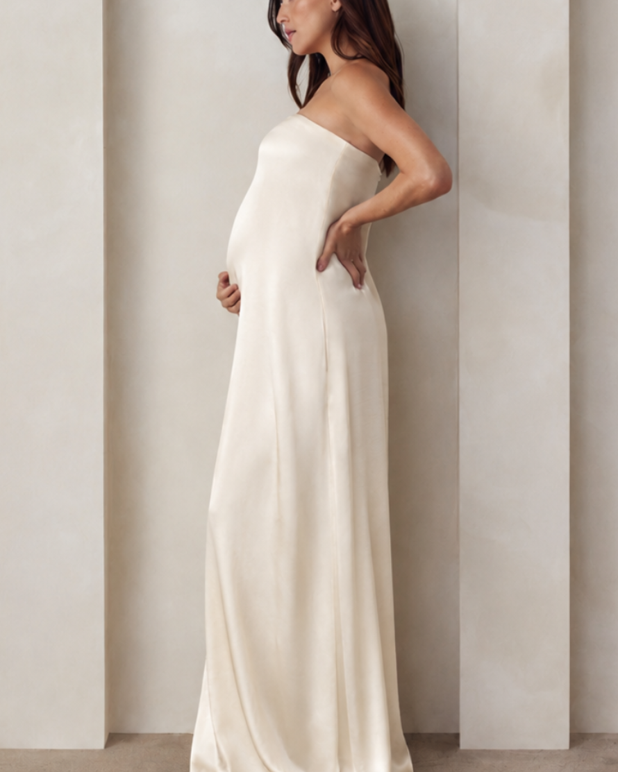Side view of a pregnant woman wearing a Bumpsuit brushed satin gown in champagne color