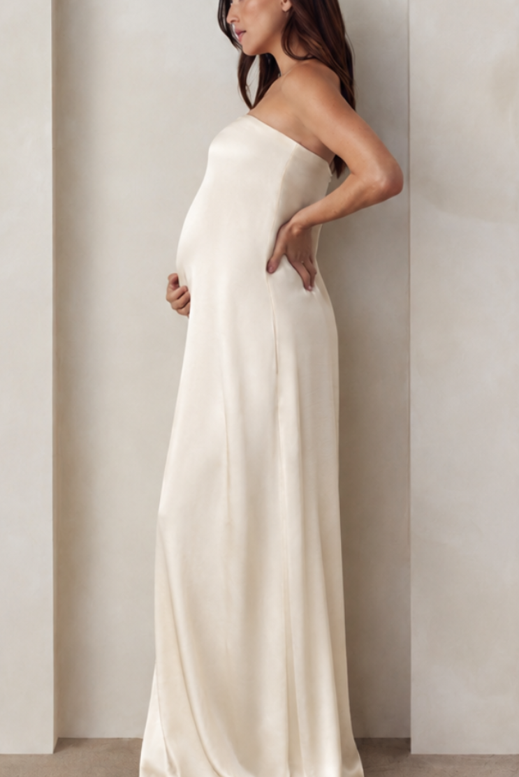 Side view of a pregnant woman wearing a Bumpsuit brushed satin strapless gown in champagne color