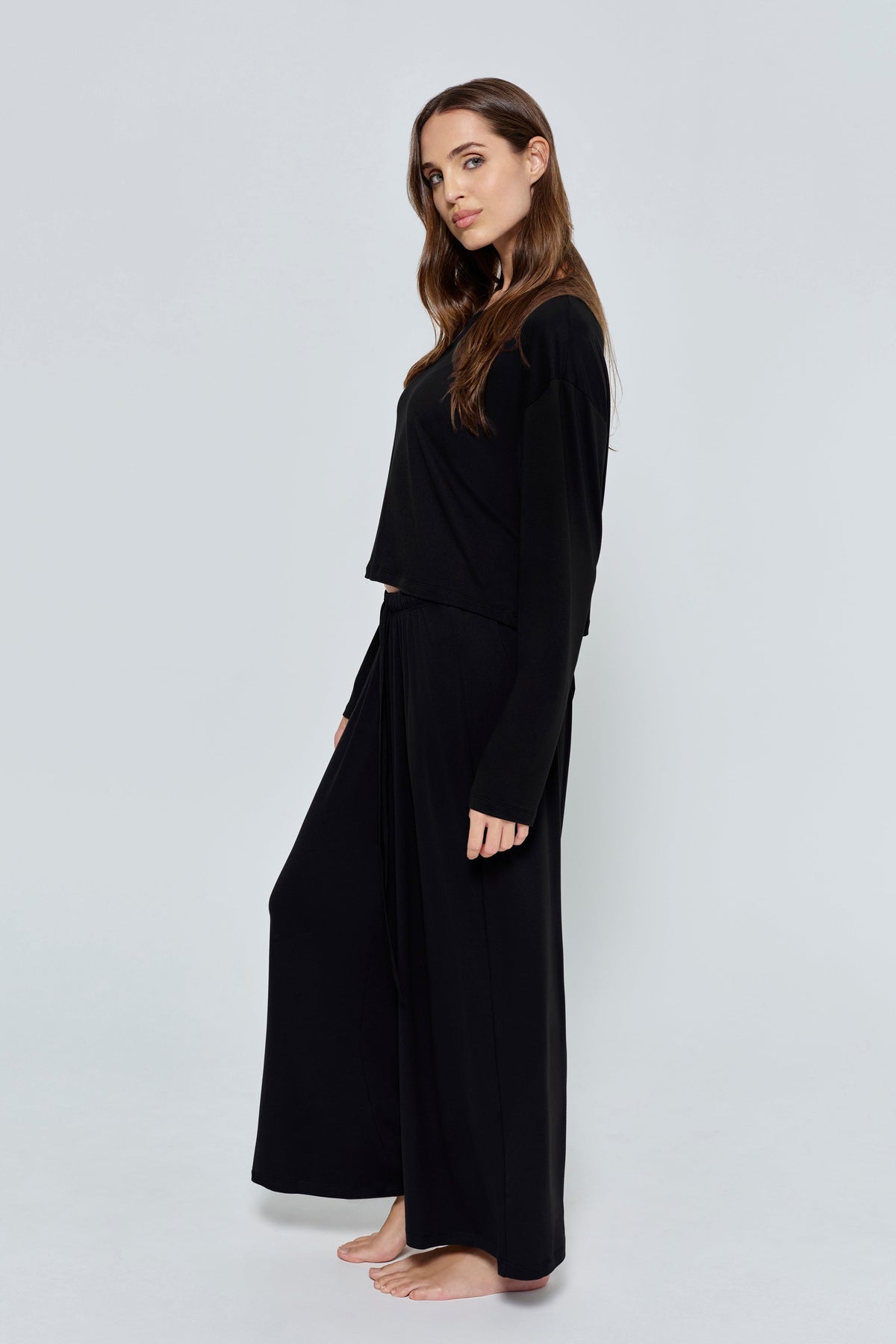 Side view of The Cloud Pant in black showcasing wide legs on a model against a light gray background