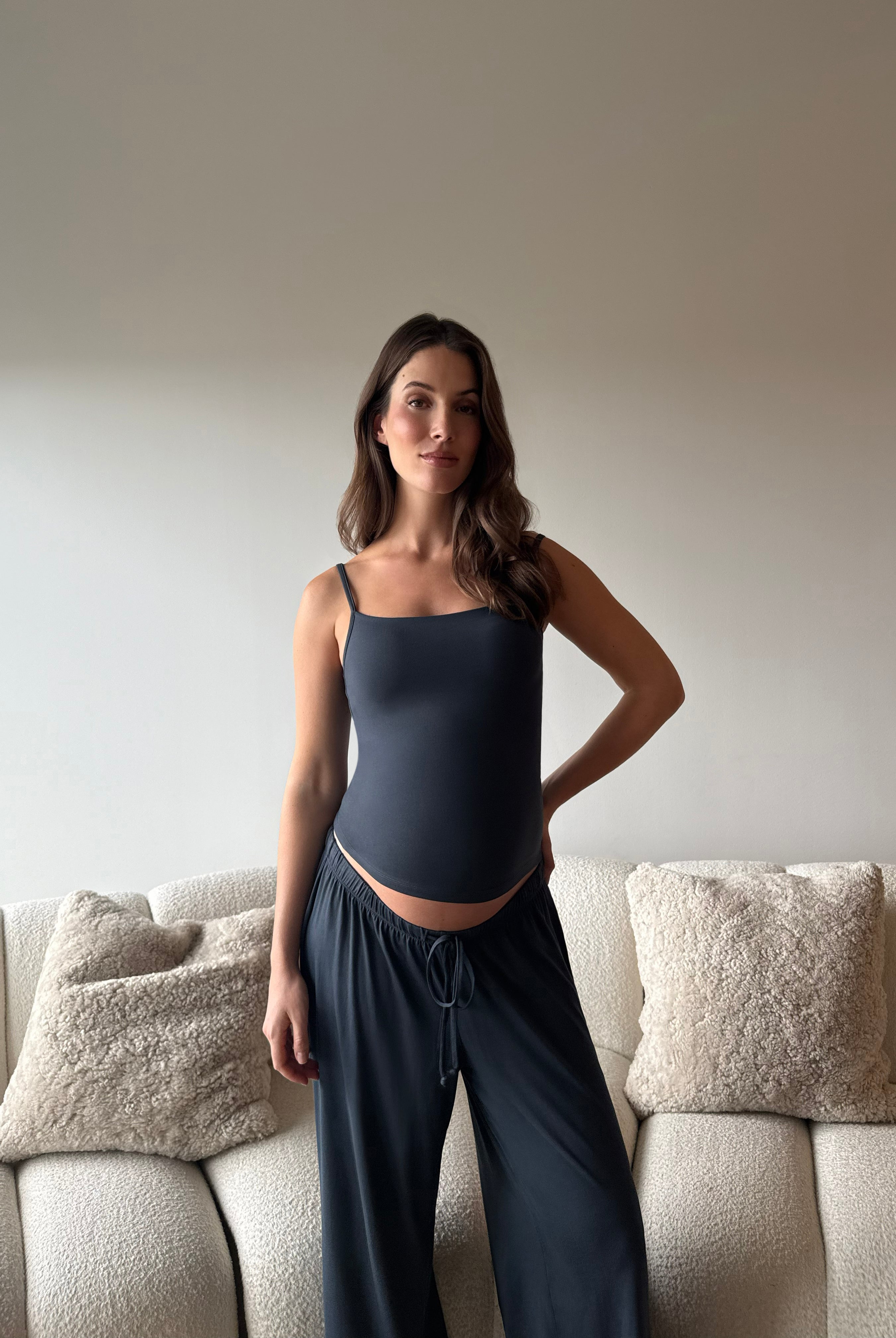 Pregnant woman wearing a Bumpsuit cloud cement blue tank top and pants in a living room.