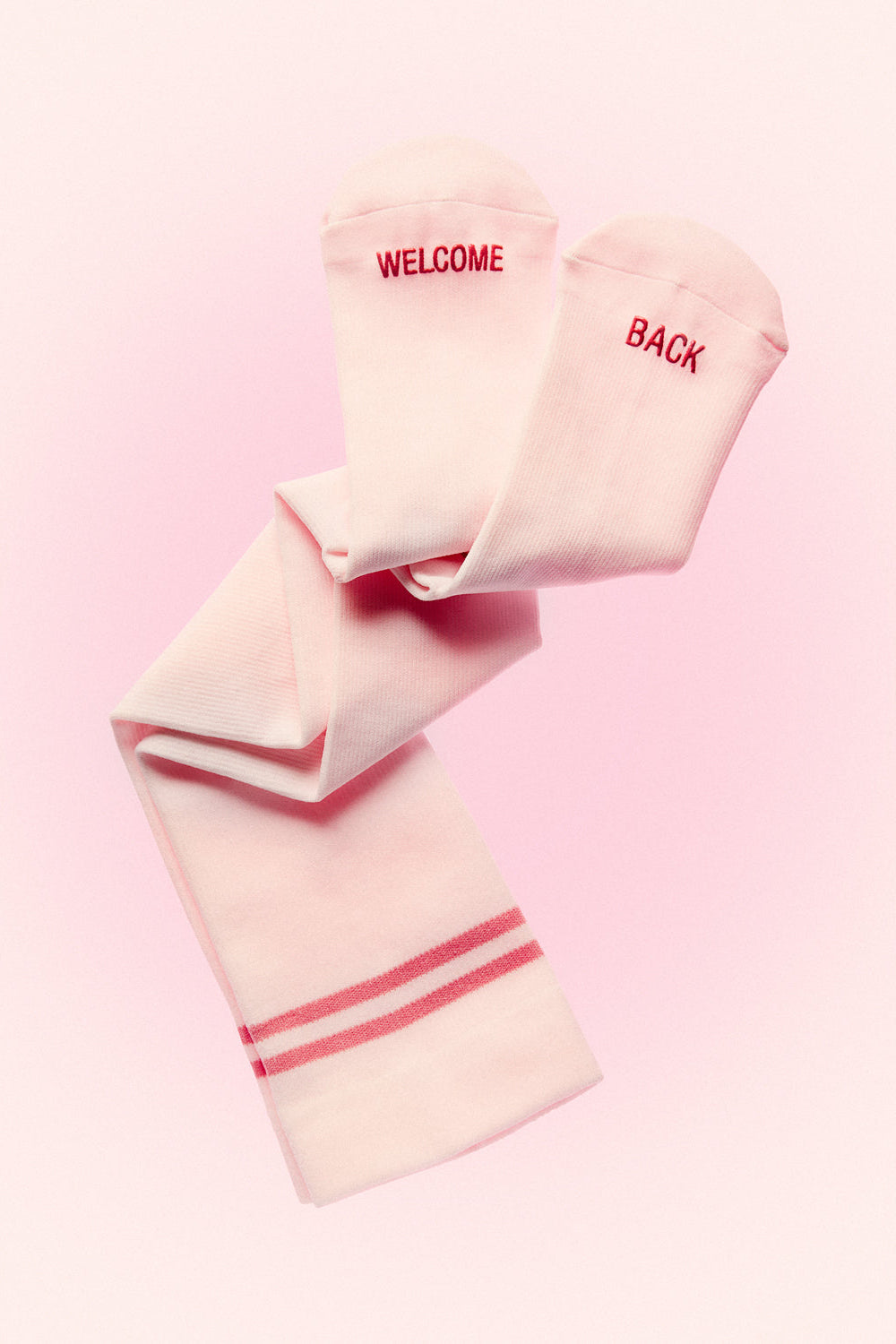 Angled view of ICE PINK compression socks showcasing WELCOME BACK text and pink stripes with a pink background