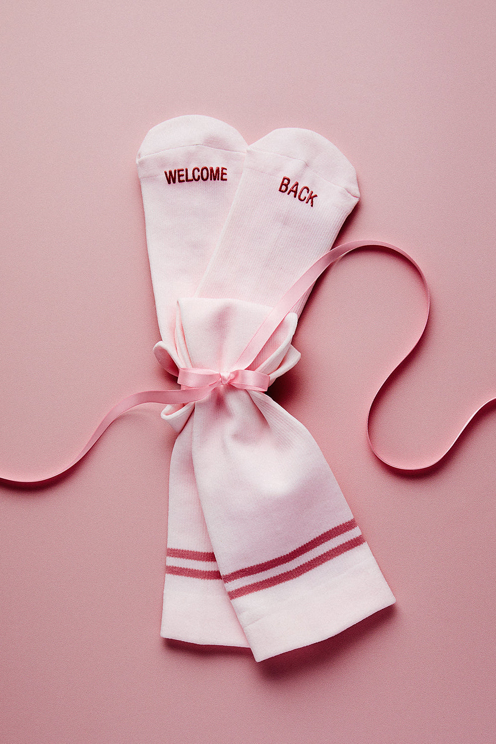 Top view of Ice Pink HOLDING IT TOGETHER compression socks showcasing WELCOME BACK text and striped cuffs in a pink gift bag