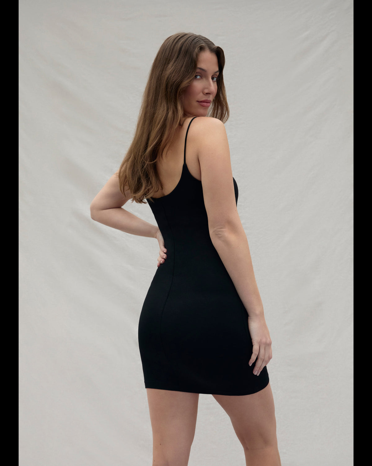Back view of a woman wearing a cotton mini black dress against a plain background
