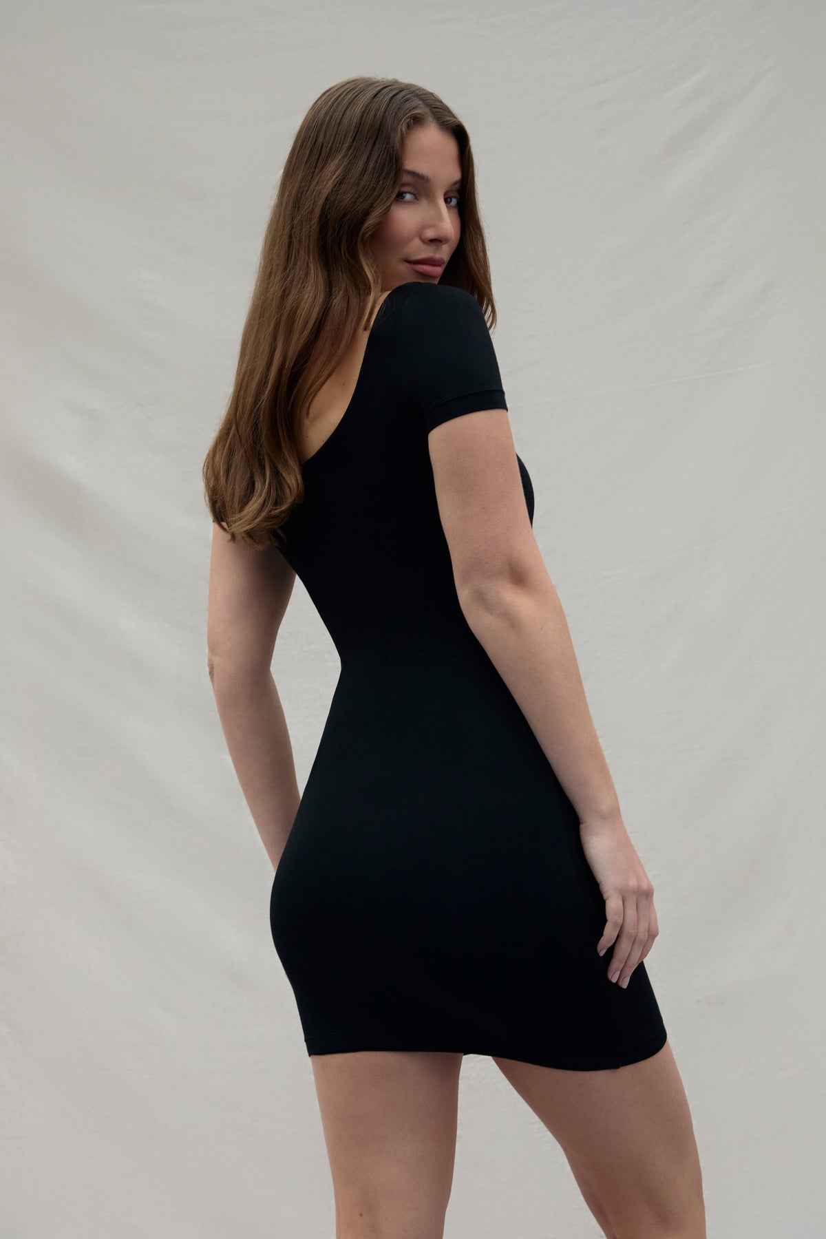 back view of a woman wearing a black Bumpsuit dress against a plain background