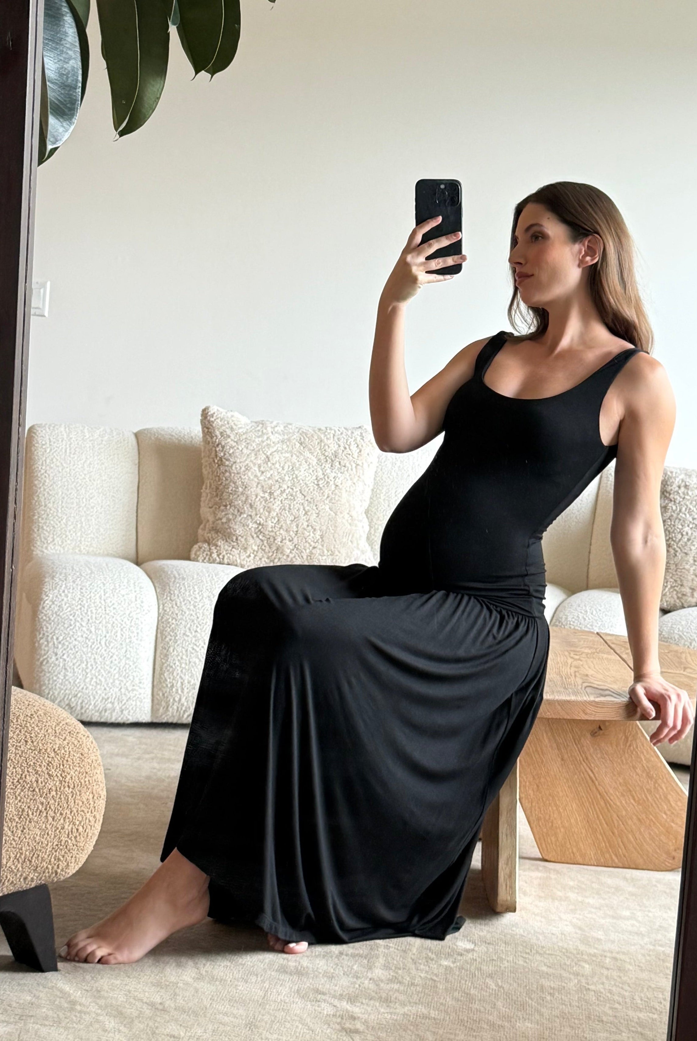 Woman in a black dress taking a mirror selfie in a living room.