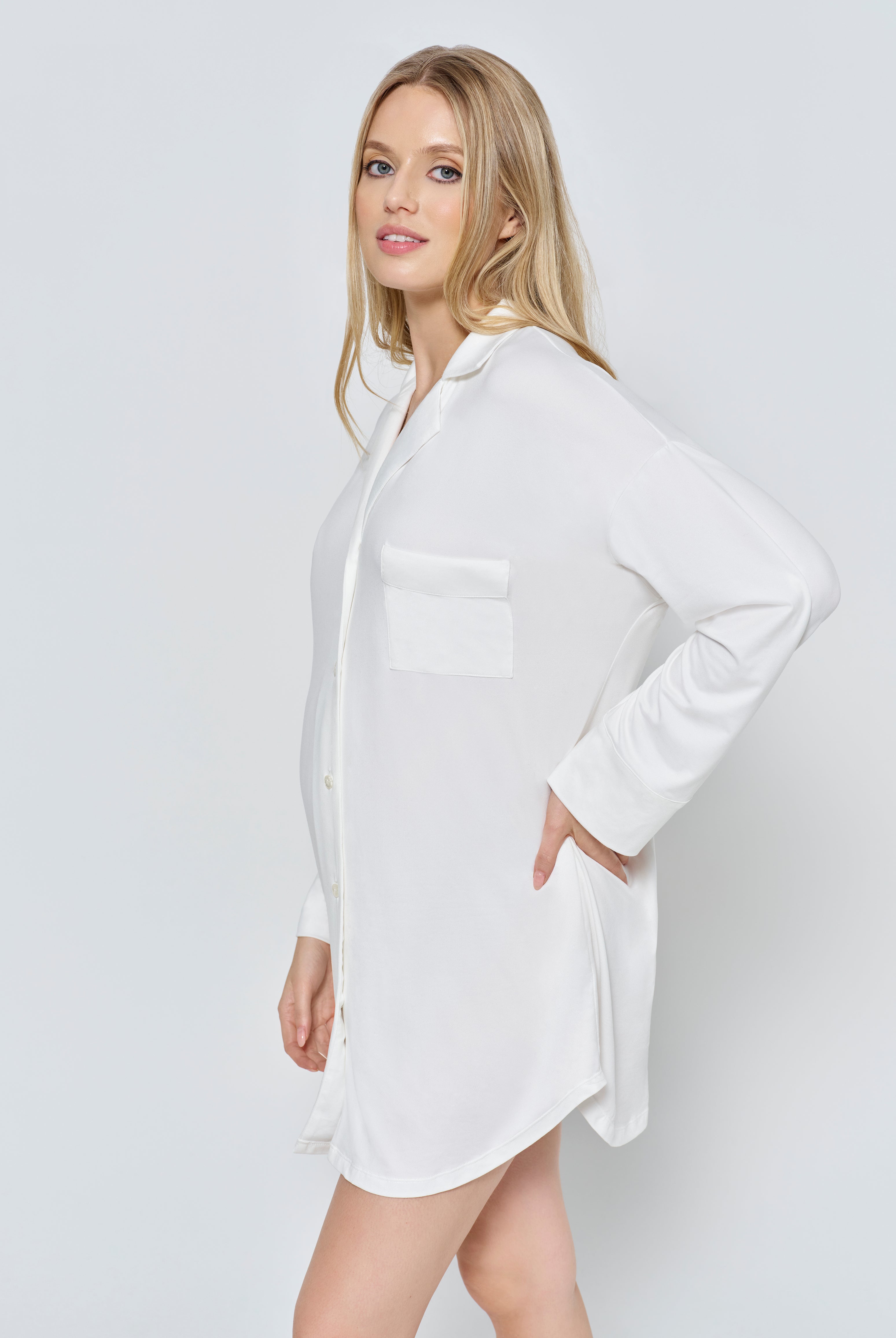 Pregnant wearing the Bumpsuit Cloud Pajama dress in ivory against a white background