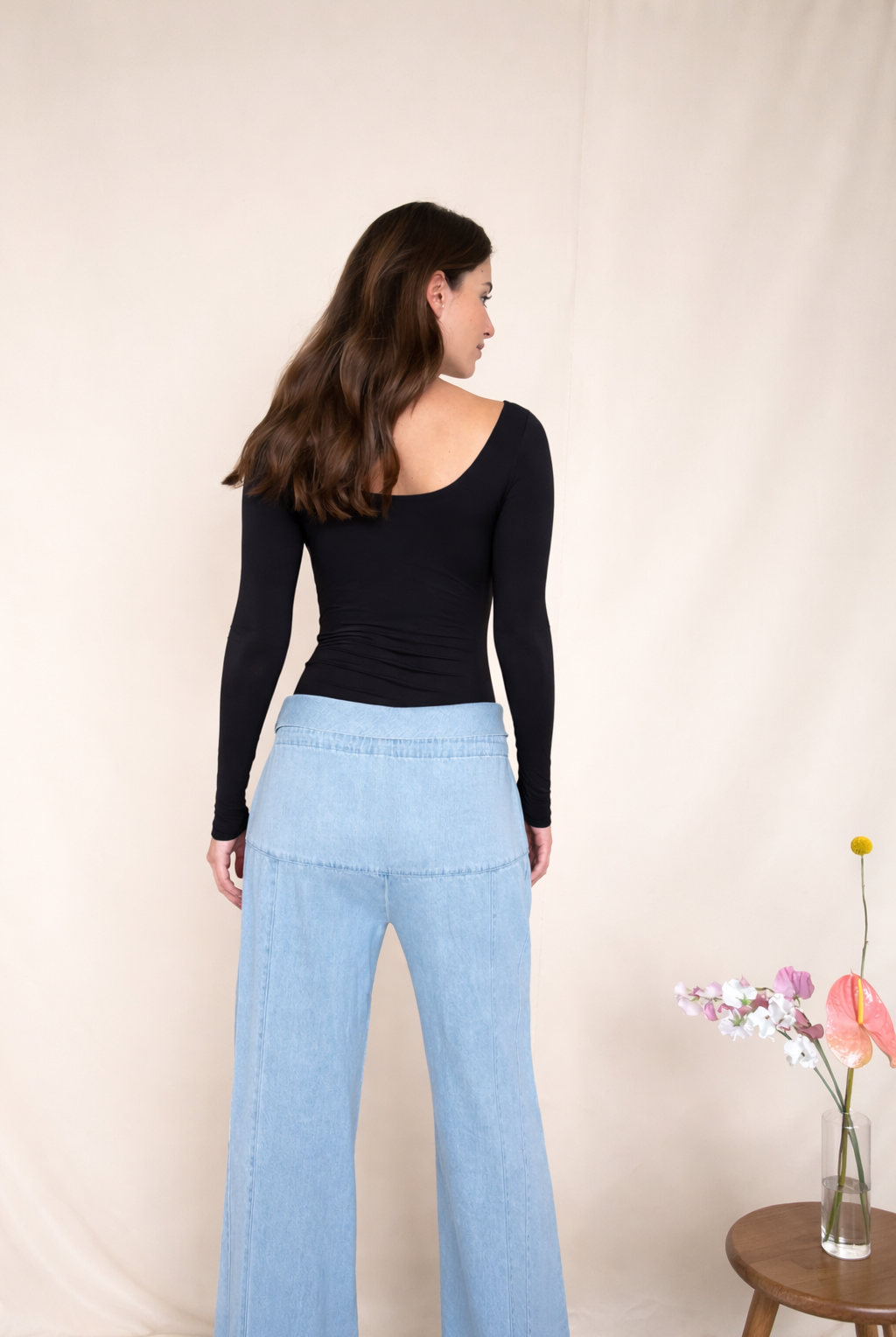 Woman wearing a black bodysuit and light blue jeans against a beige background