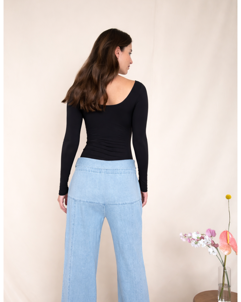 Woman wearing a black bodysuit and light blue jeans against a beige background